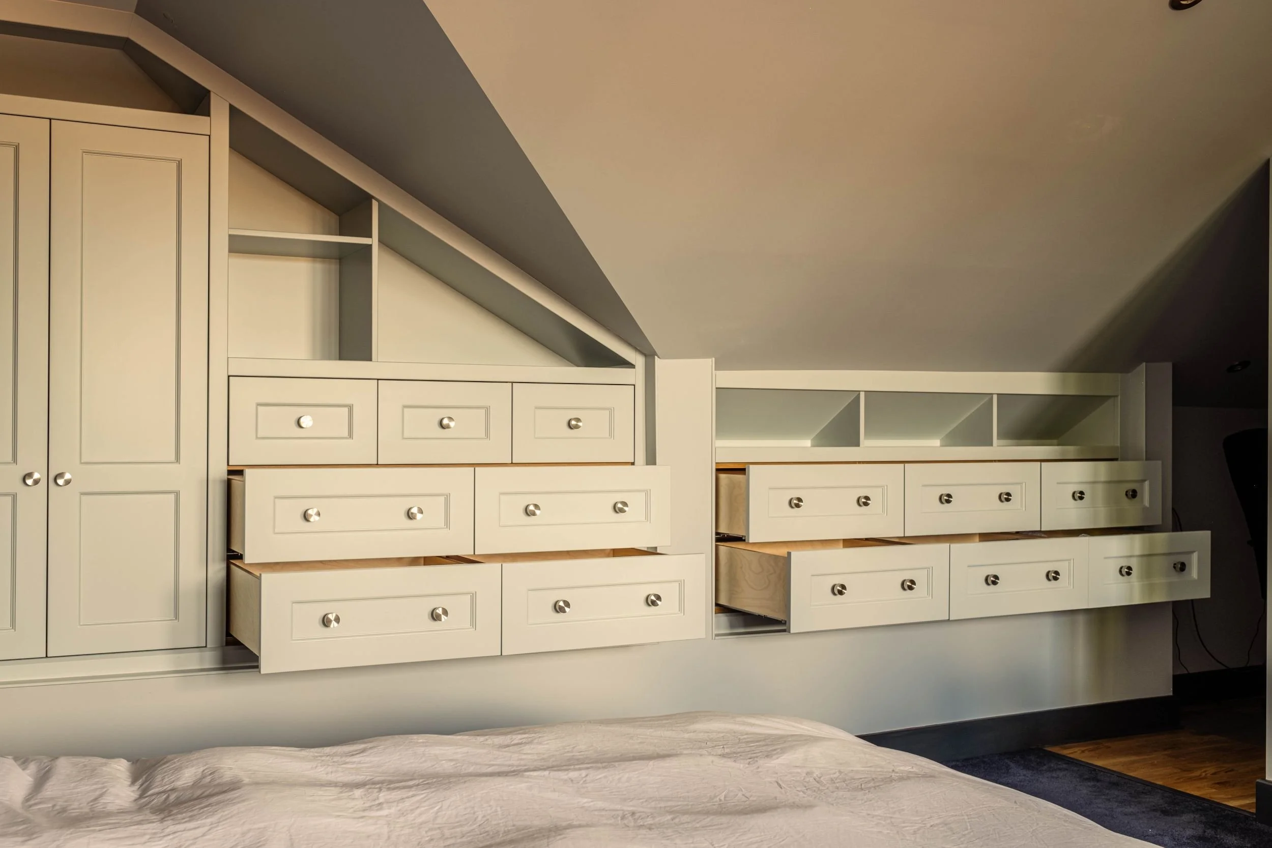 A made to measure wardrobe with open shelving and lots of drawers, some of which are open, all fitted into a loft space with sloping ceilings.