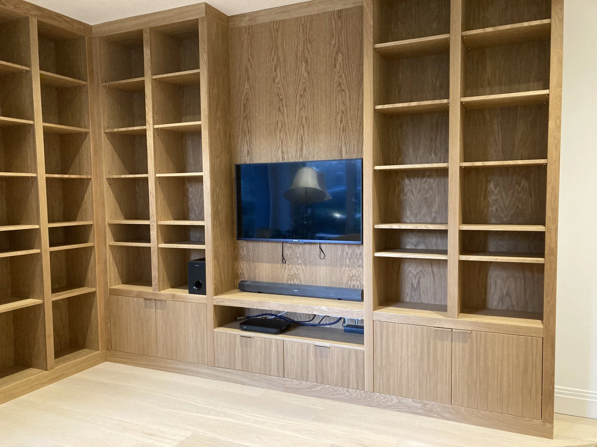 Large made to measure bespoke media unit made from oak veneer and solid oak. media unit consists of a base unit cupboard section and a top unit section with adjustable shelving.