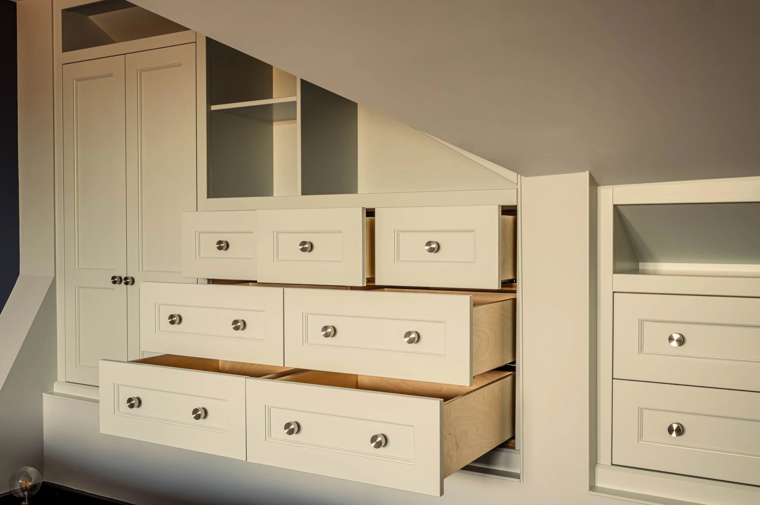 A made to measure wardrobe with open shelving and lots of drawers, some of which are open, all fitted into a loft space with sloping ceilings.