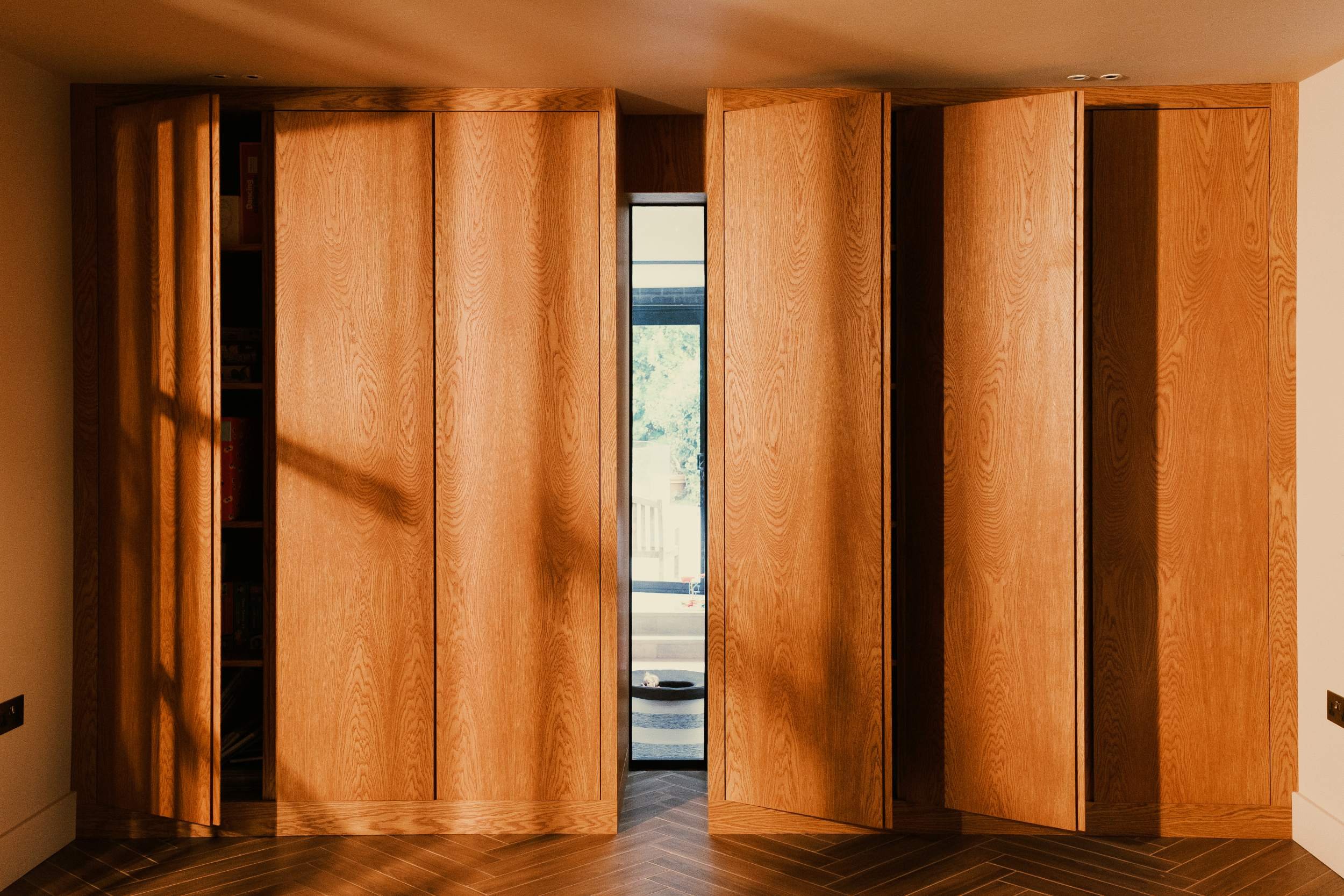 Two made to measure cupboards made from stained oak veneered boards. The cupboards are a mid century design with finger pull handles molded into the doors. The doors are slightly open.