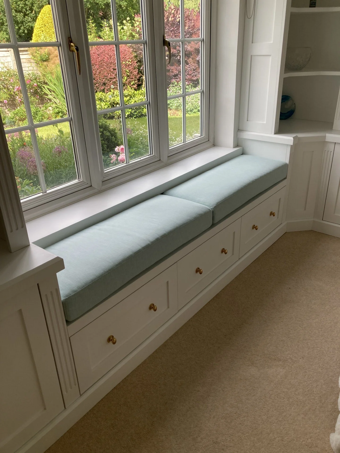 A made to measure window seat painted white with blue cushions. The seat has pull out drawers below.