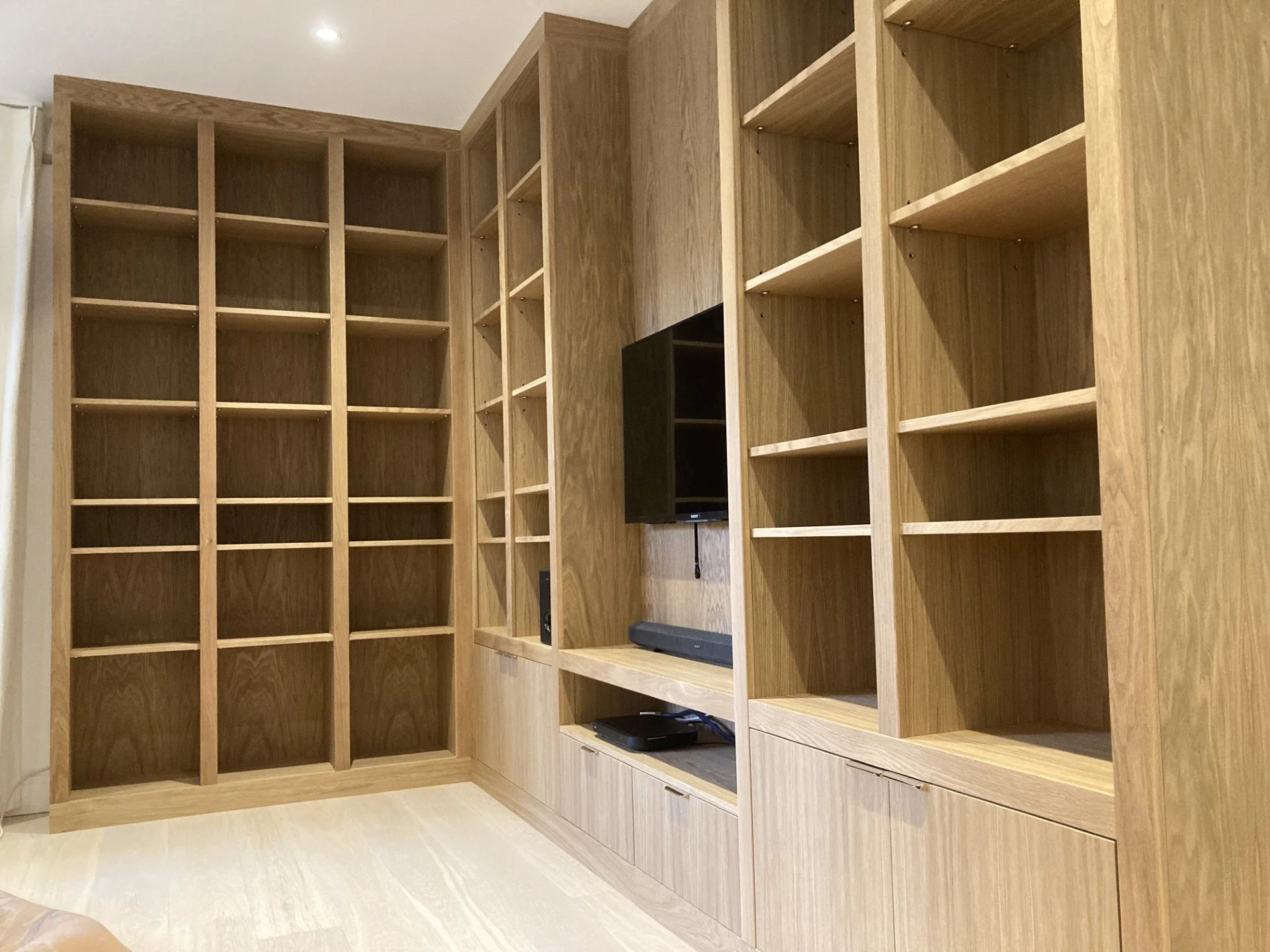 Close up of a made to measure bespoke media unit made from oak veneered boards and solid oak. Media unit consists of cupboards and adjustable shelving.