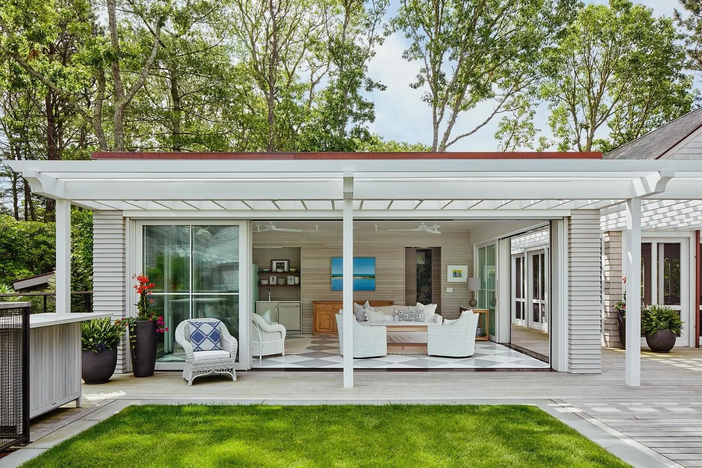 The sides of our Cape Cod Poolhouse project open up fully, creating a sense of openness during the warmer months. A pergola unites the kitchenette and changing area space with a screened-in porch for entertaining, while boat storage space is tucked a