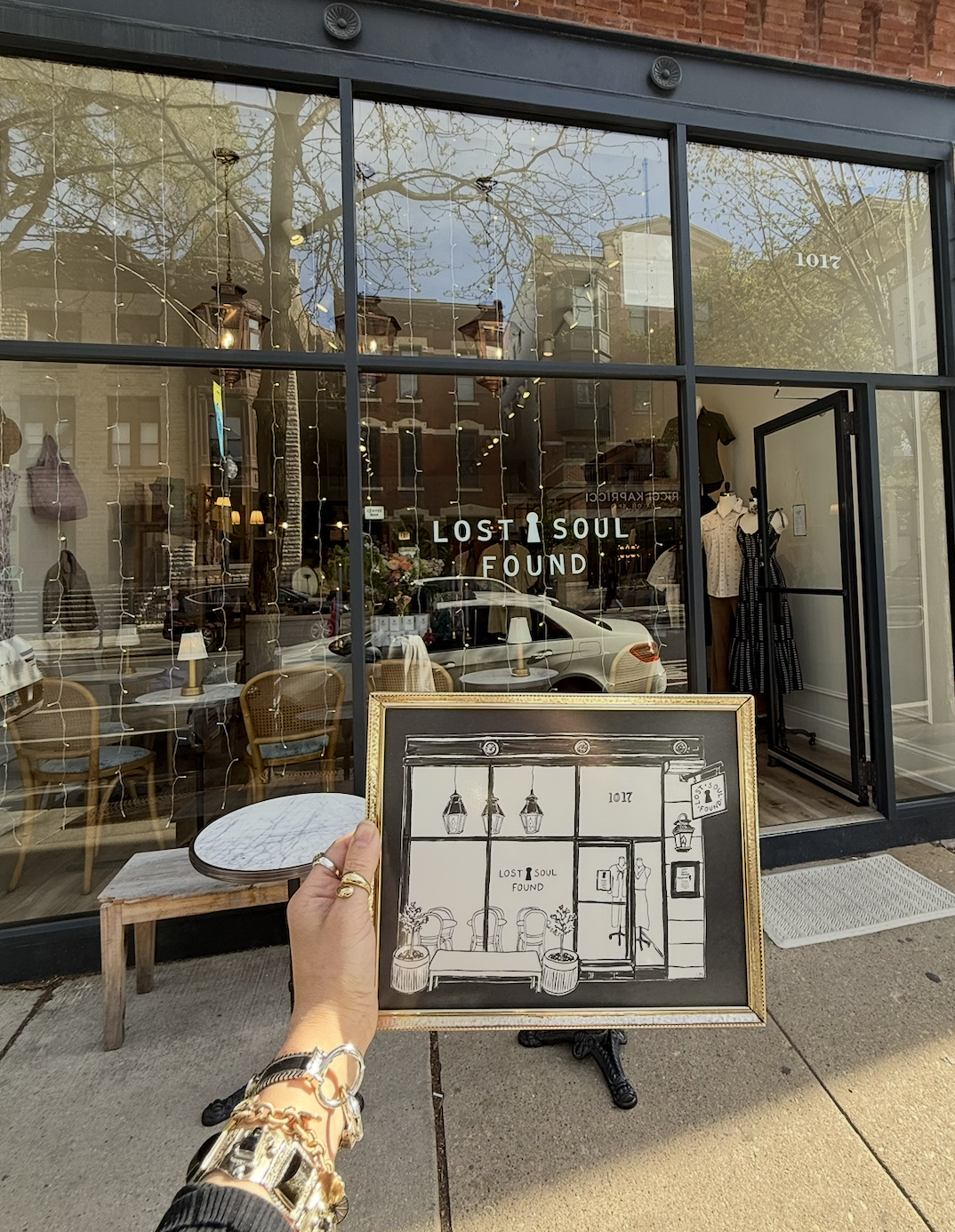 Person holding a framed art piece with a storefront in the background that says 'LOST SOUL FOUND'.