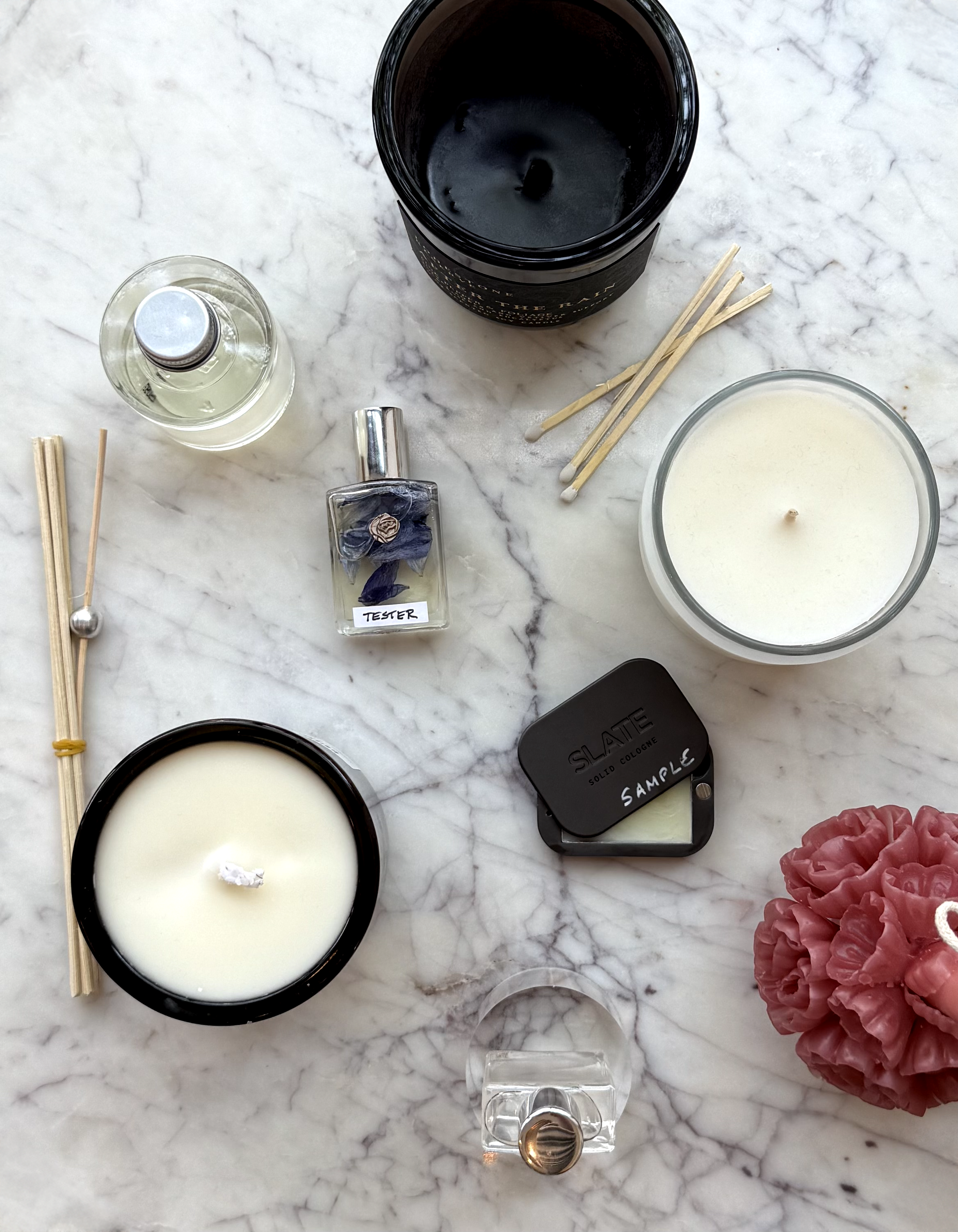 Various candles, candles, reed diffusers, and perfume bottles arranged on a marble surface.