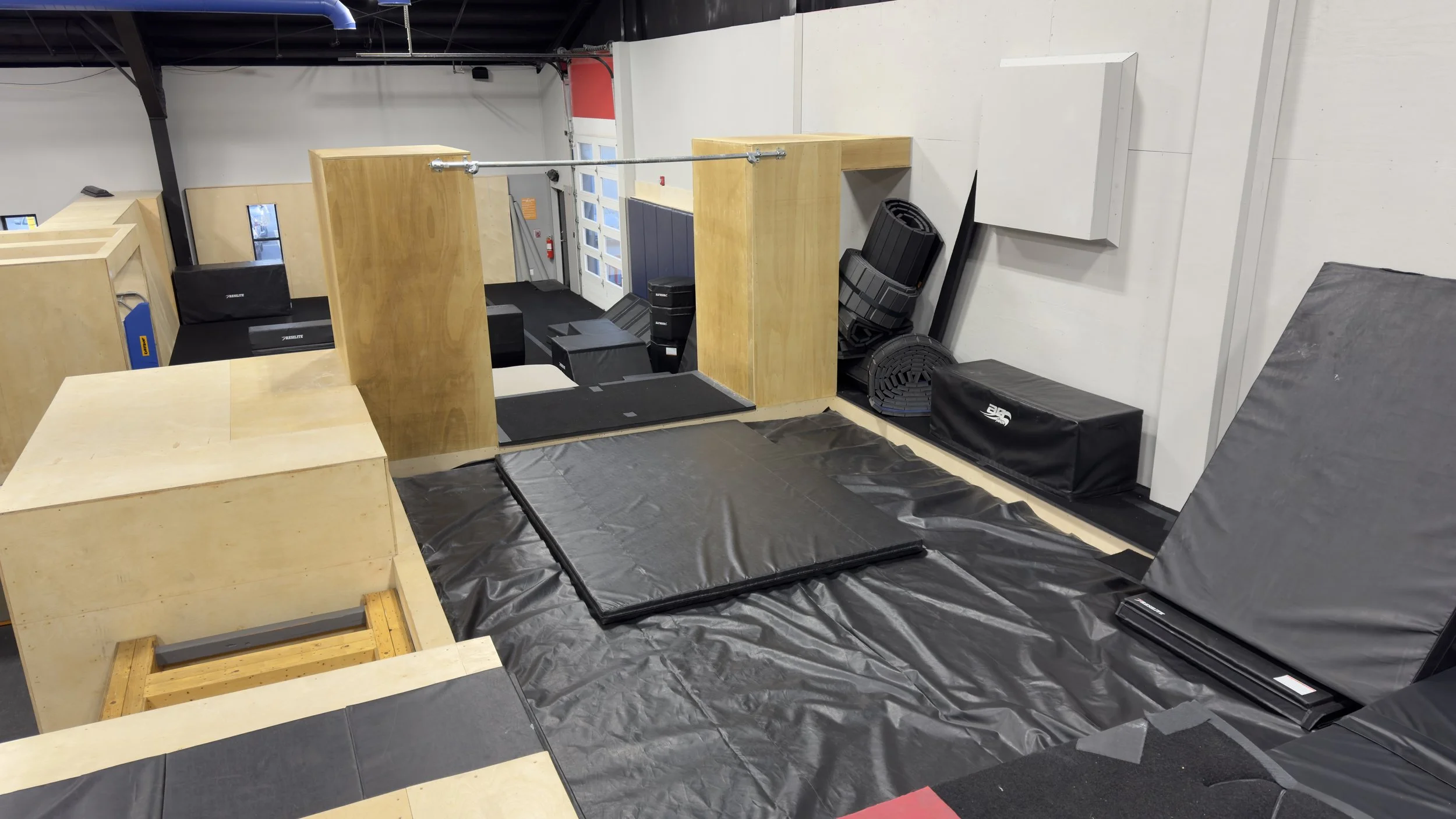 Indoor parkour training area with padded mats, wooden structures, foam blocks, and black padding for safety.