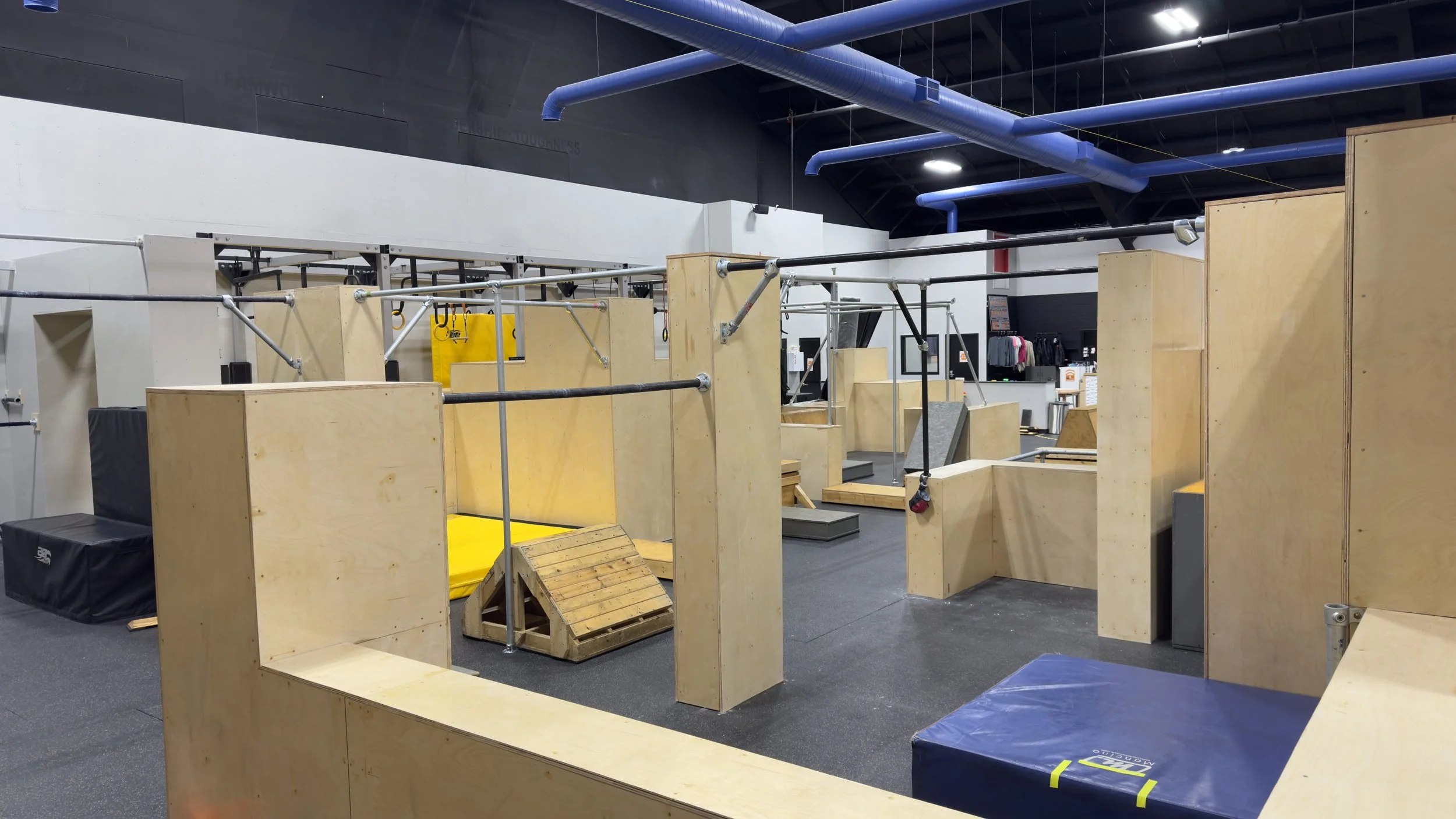 Indoor parkour training area with wooden structures, foam pads, and metal bars for obstacle courses.
