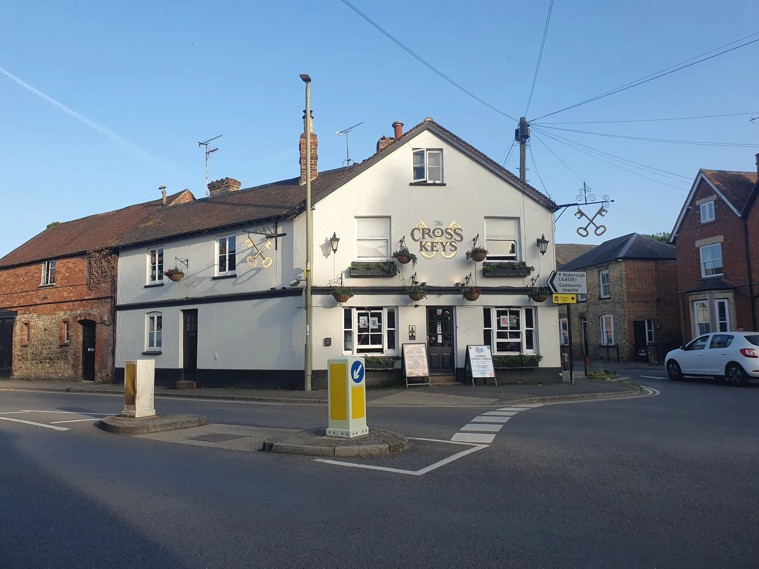 A photo of the Cross Keys Pub Thame showing the white building with the Cross Keys pub sign on the front of the building. The pub sits on a mini roundabout.