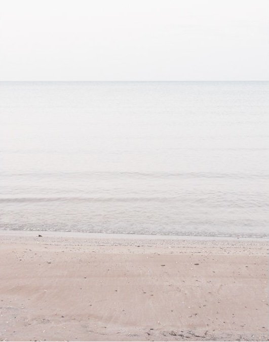 A calm beach scene with light-colored sand and gentle ocean waves under a pale sky.