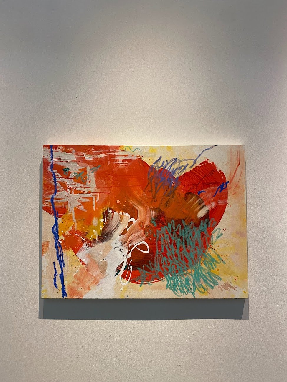 A 40" x 30" abstract mixed media painting with bold red accented with oil pastel marks in mint and cobalt blue. Pictured hanging at the Ford Gallery in Portland, OR.