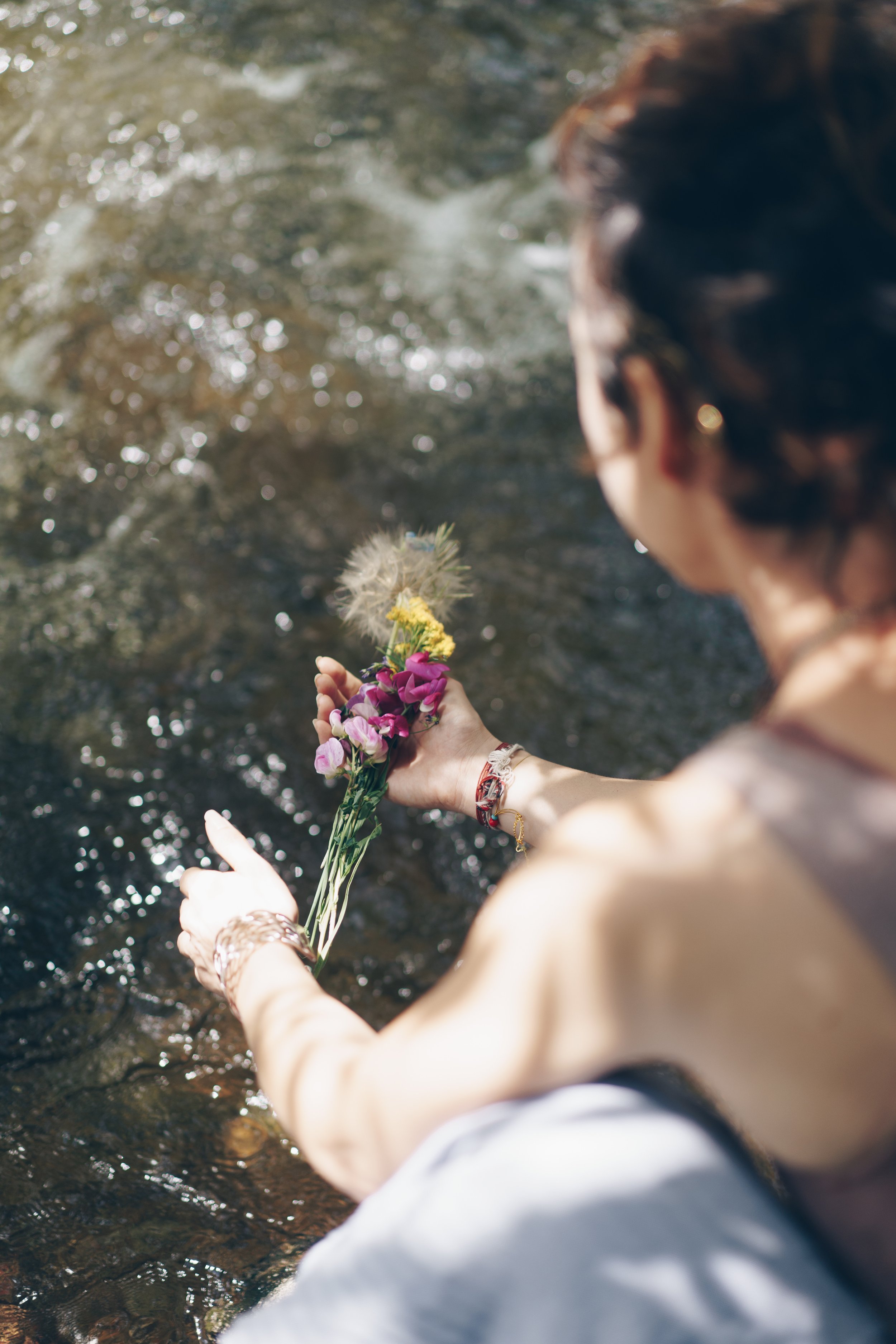 Woman kneeling by a sparkling stream holding a small bouquet of wildflowers