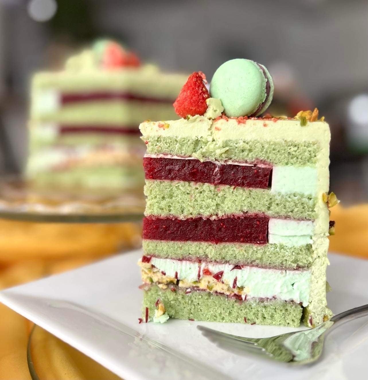 A sliced green cake with green and red cream fillings with macaroons, nuts and cranberry toppings.