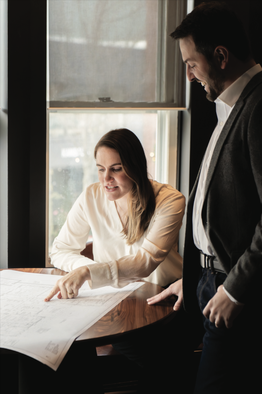A man and a woman discussing architectural plans at a table near a window in an office.