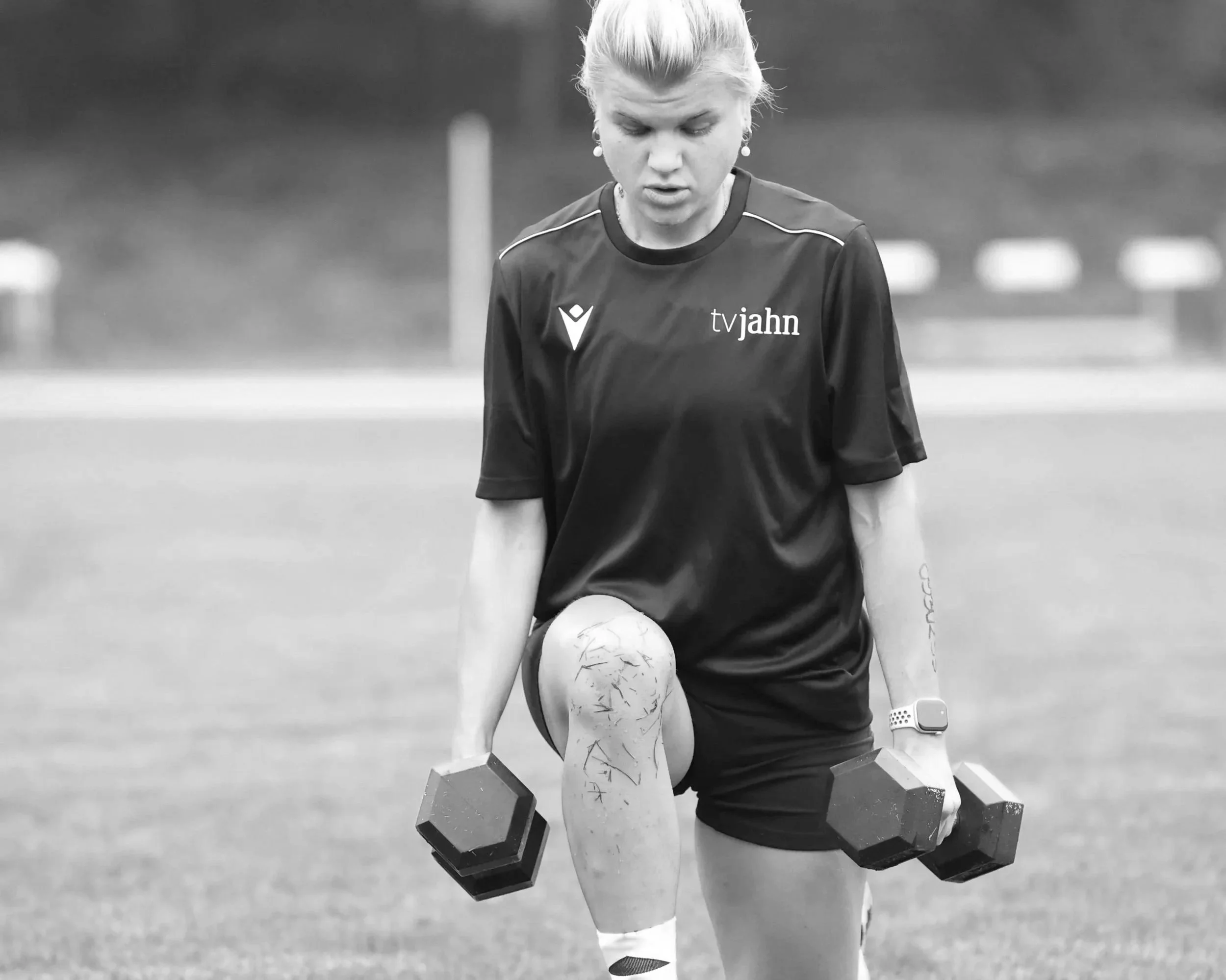 A woman in athletic clothing lifting dumbbells during outdoor workout.