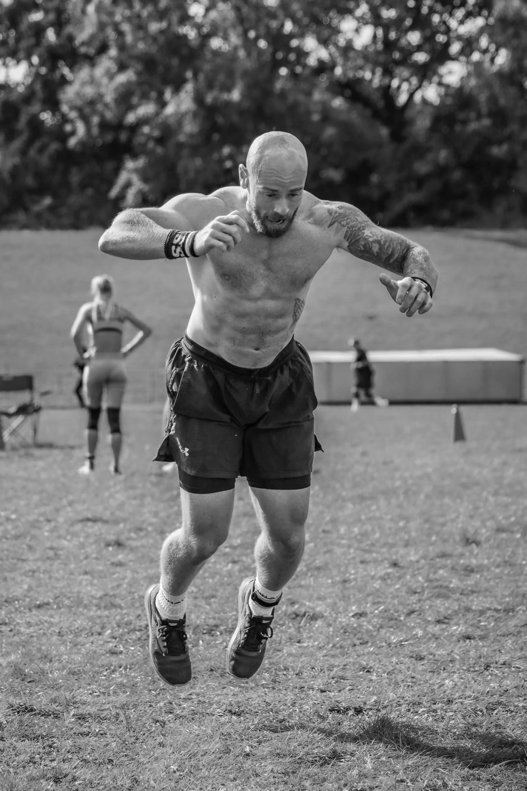 Man jumping outdoors with tattoos and shorts, exercise scene