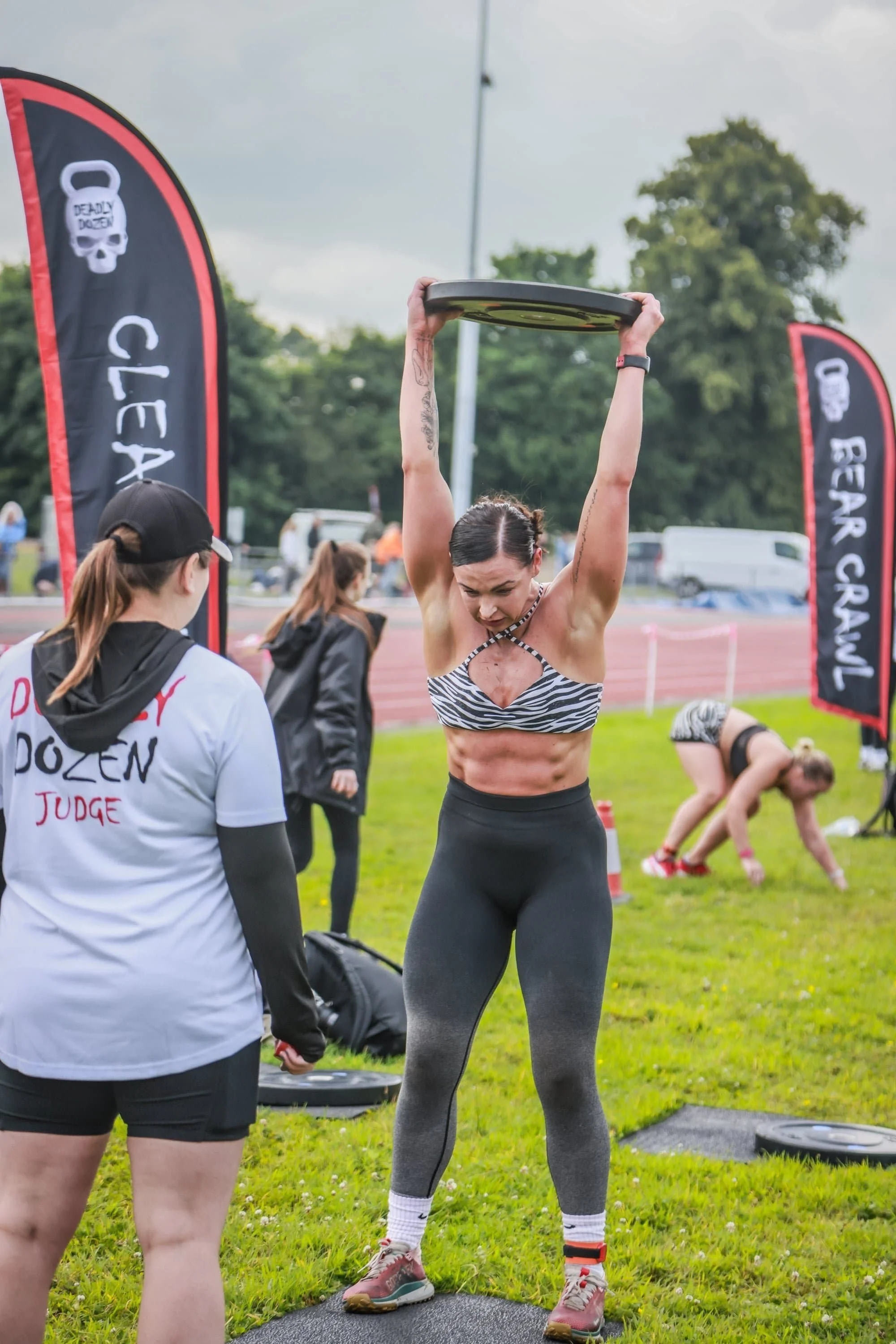 Female athlete at a Deadly Dozen event performing clean & press with weight plate