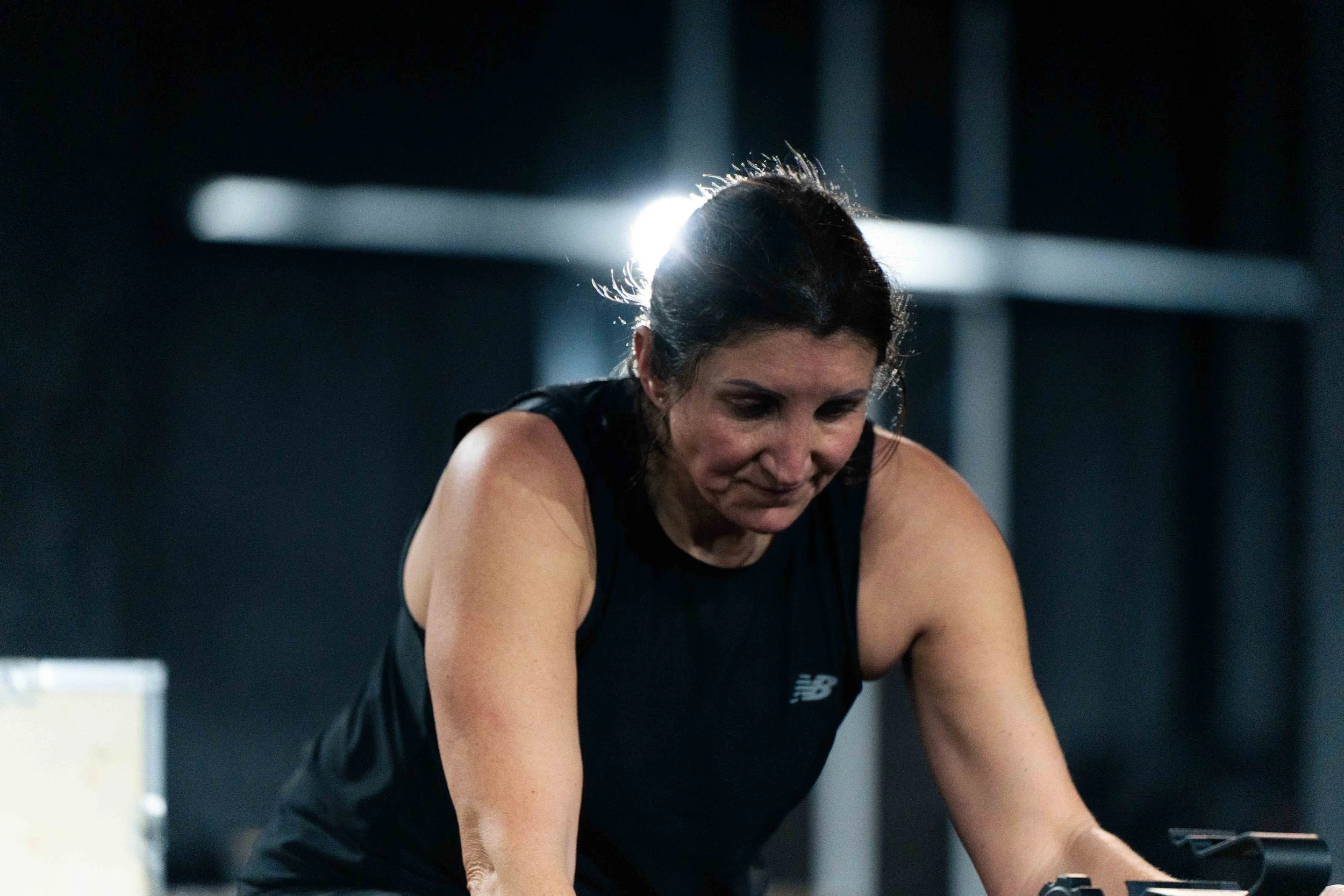 Woman exercising in a gym, wearing black sports attire, with a focused expression.