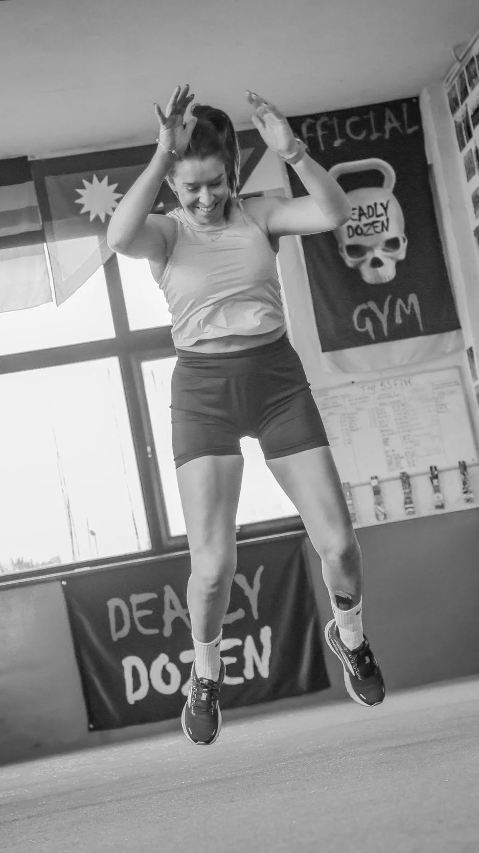 Woman jumping in a gym with banners and flags, wearing athletic clothing.