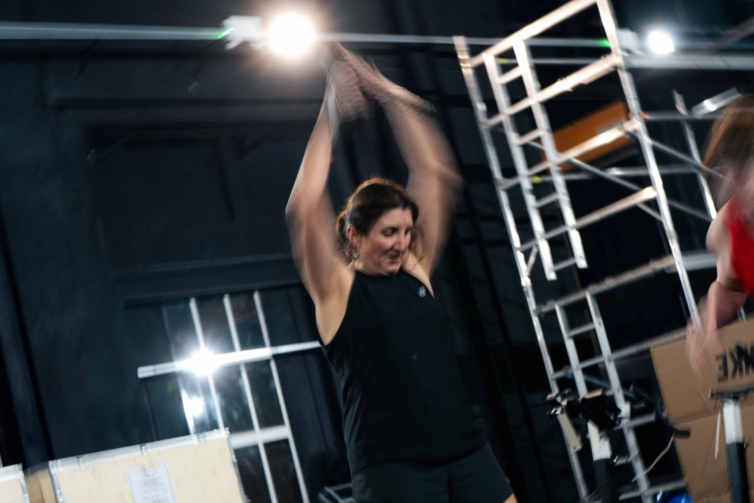 Woman in black sleeveless top and black shorts practicing flagging in a gym