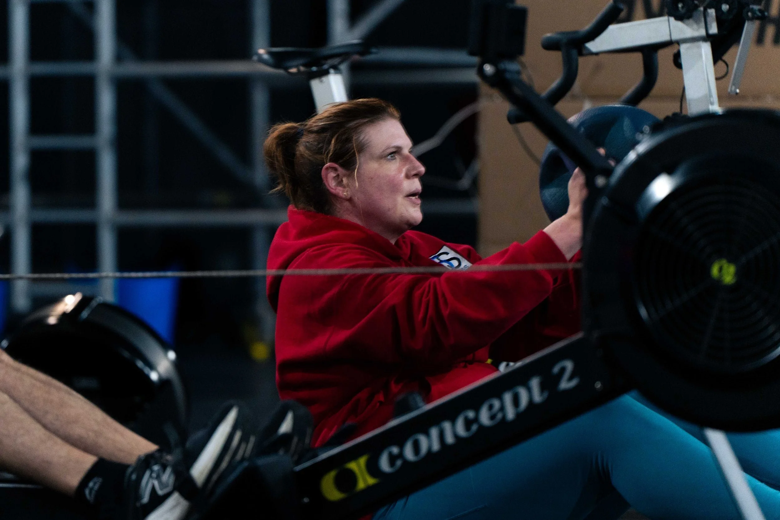 A woman in a red hoodie using a Concept2 rowing machine indoors.