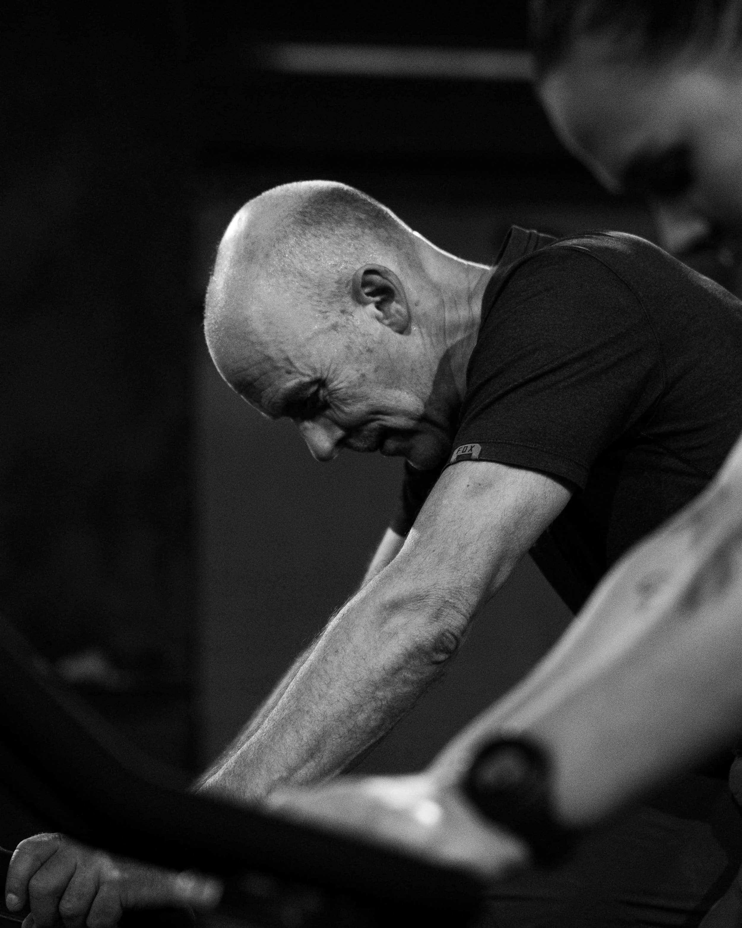 Black and white photo of a man with a shaved head smiling while exercising on a rowing machine.