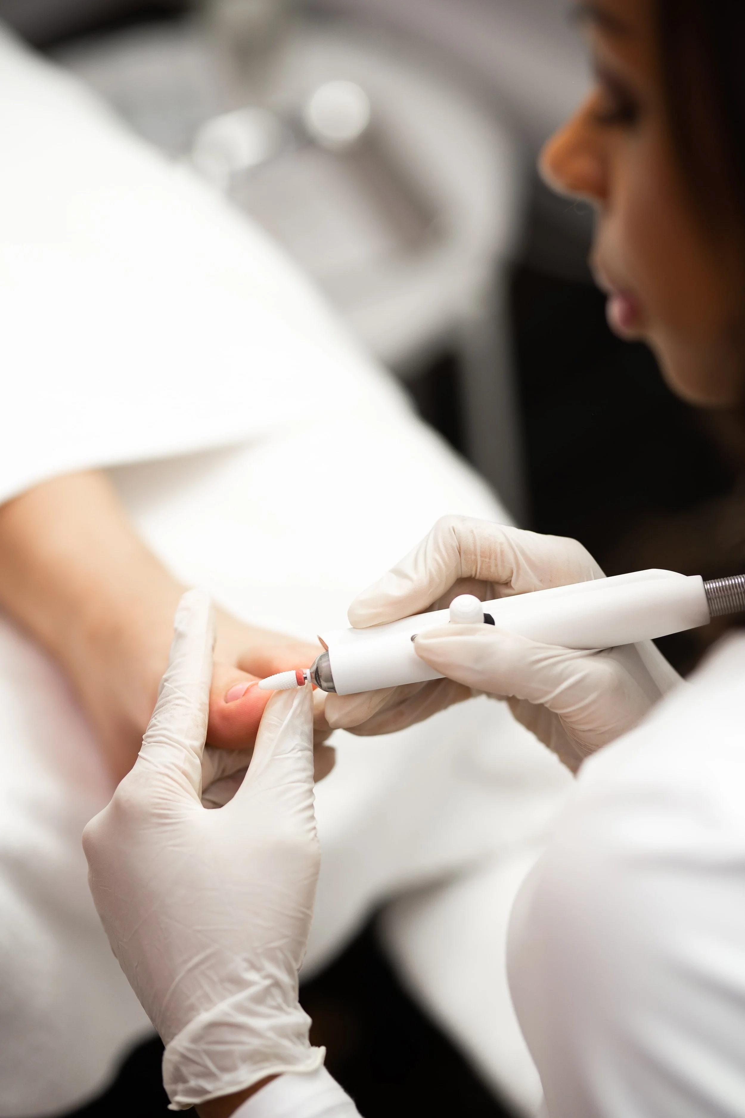 Nahaufnahme einer medizinischen Fußpflegebehandlung mit Handschuhen und elektrischem Fräser an einem Zeh