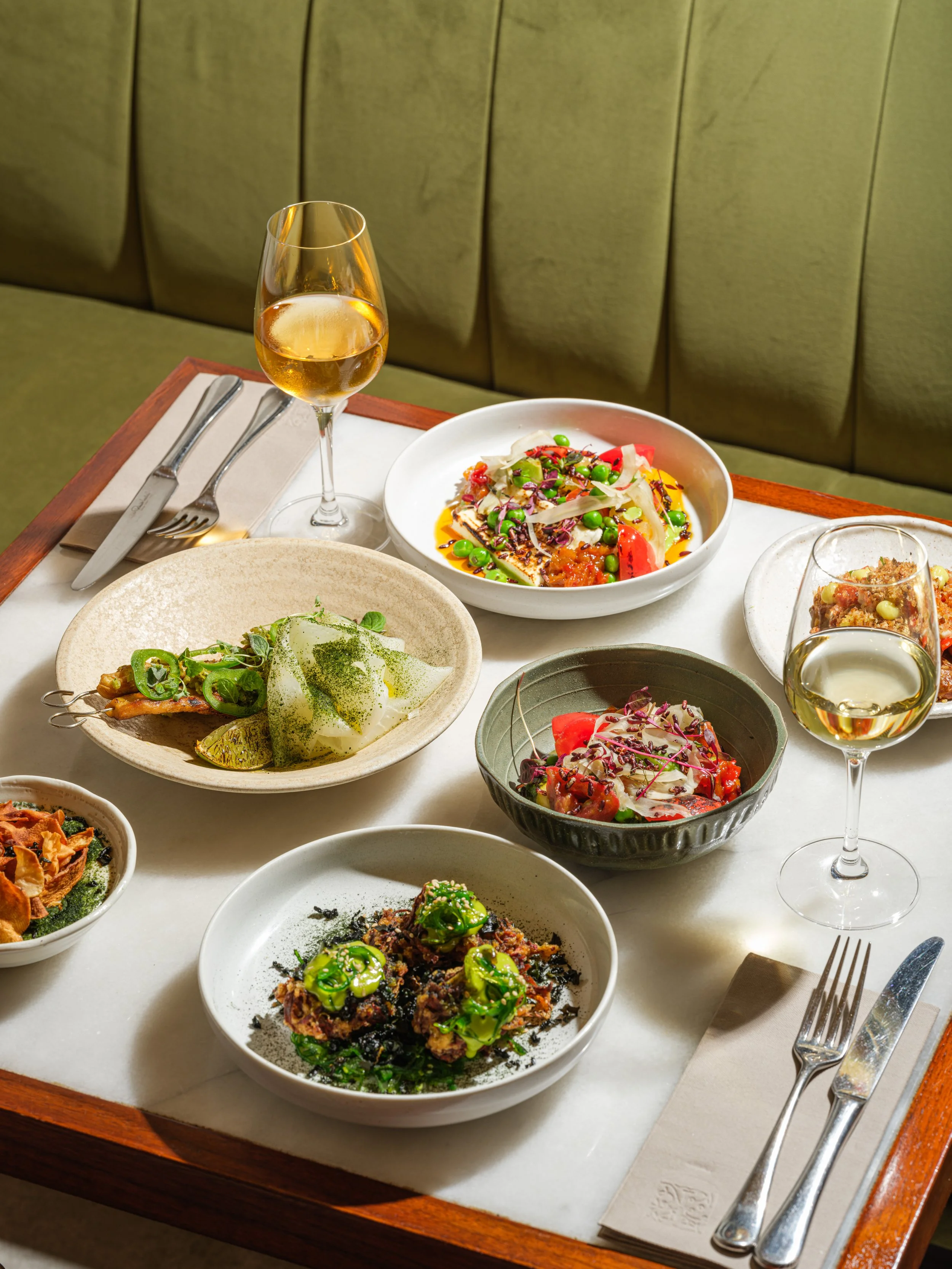 A dining table with various Asian dishes and two glasses of white wine.