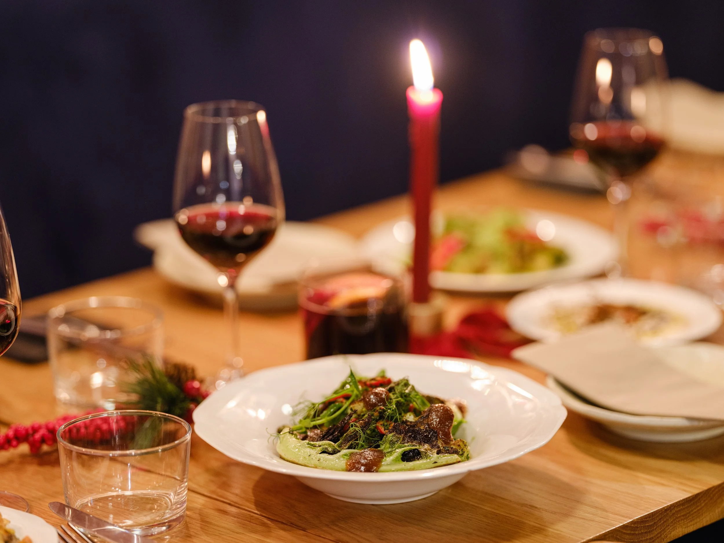 A dinner table set with glasses of red wine, a lit red candle, plates of salad, and other dishes for a festive meal.