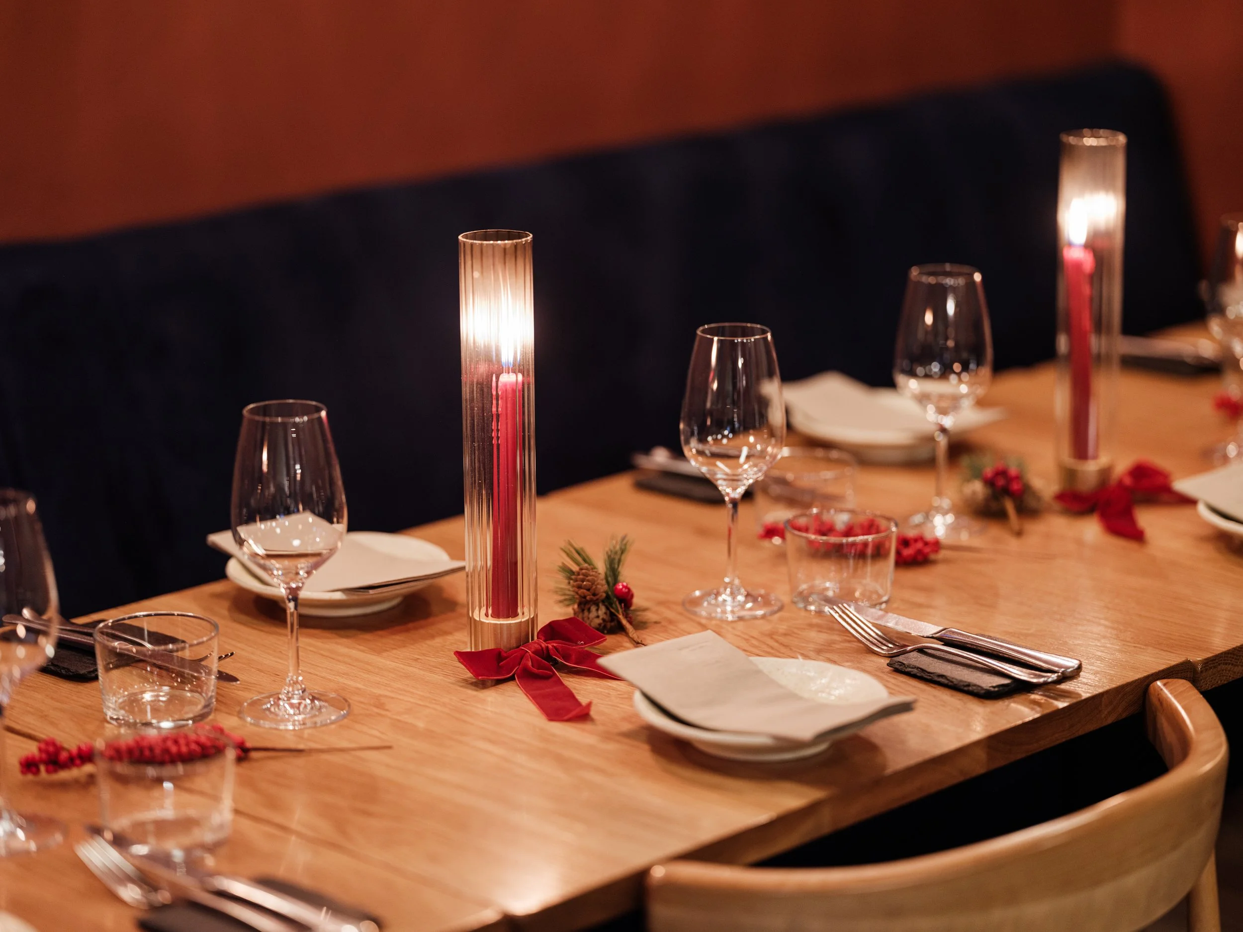 A decorated dining table with candles, glasses, plates, silverware, napkins, and holiday decorations.