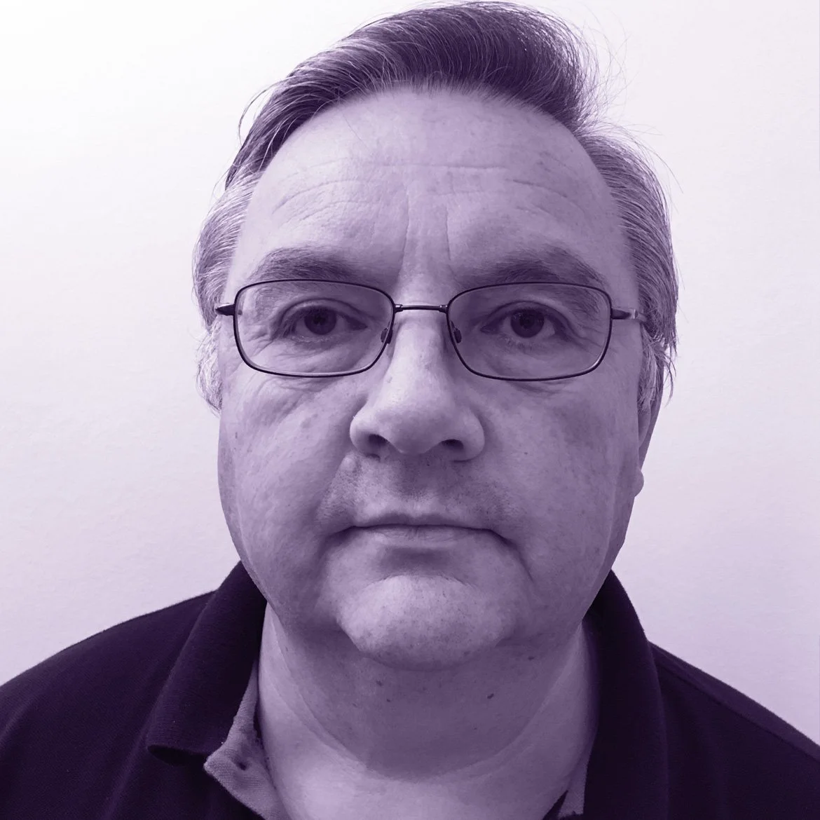 Close-up of a middle-aged man with glasses, short gray hair, and a serious expression, against a plain light background.