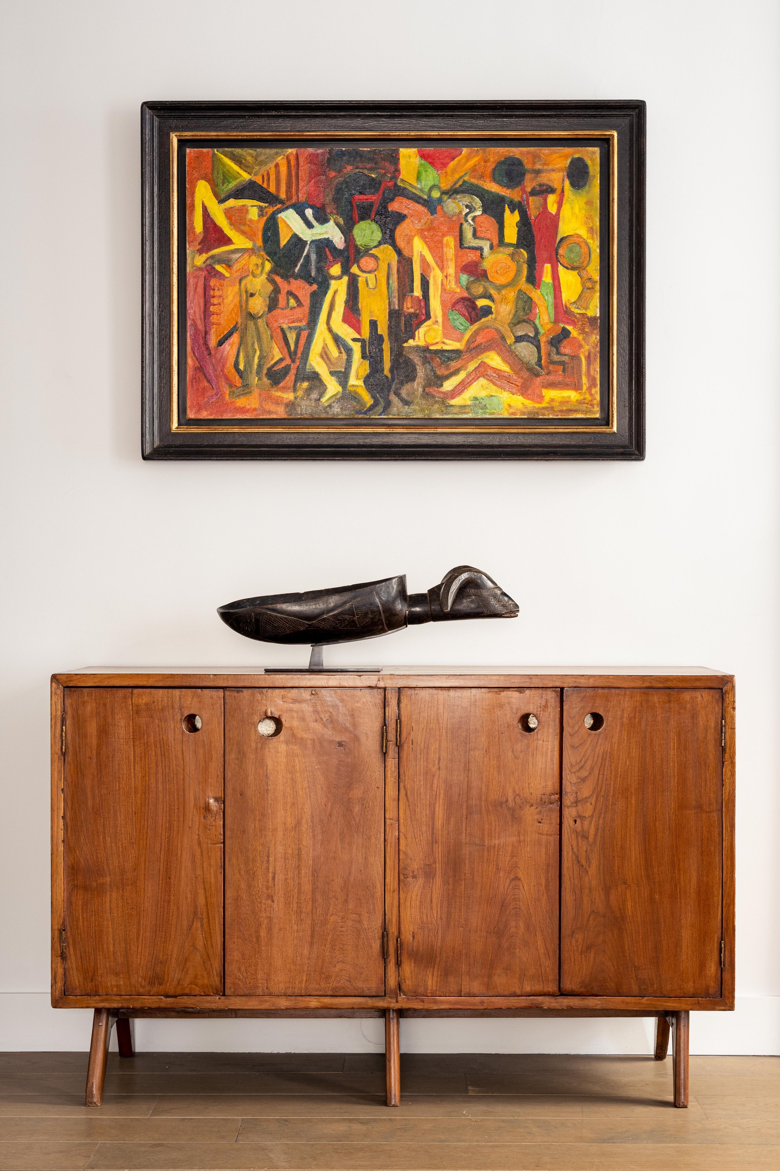 Une peinture abstraite colorée dans un cadre noir, un meuble en bois avec une sculpture en bois sur le dessus.
