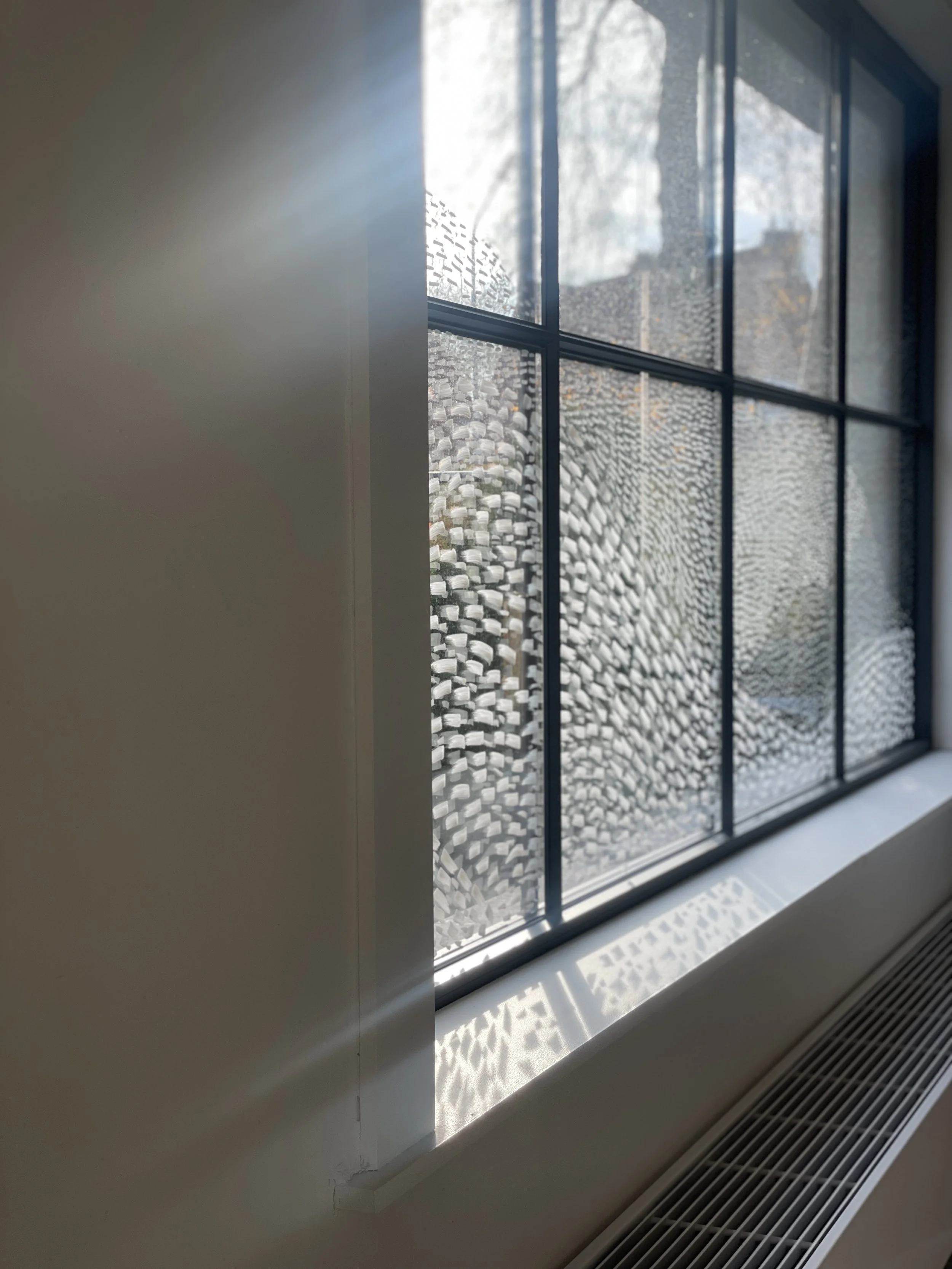 Close-up of a window with textured glass, showing sunlight and shadows on the window sill.