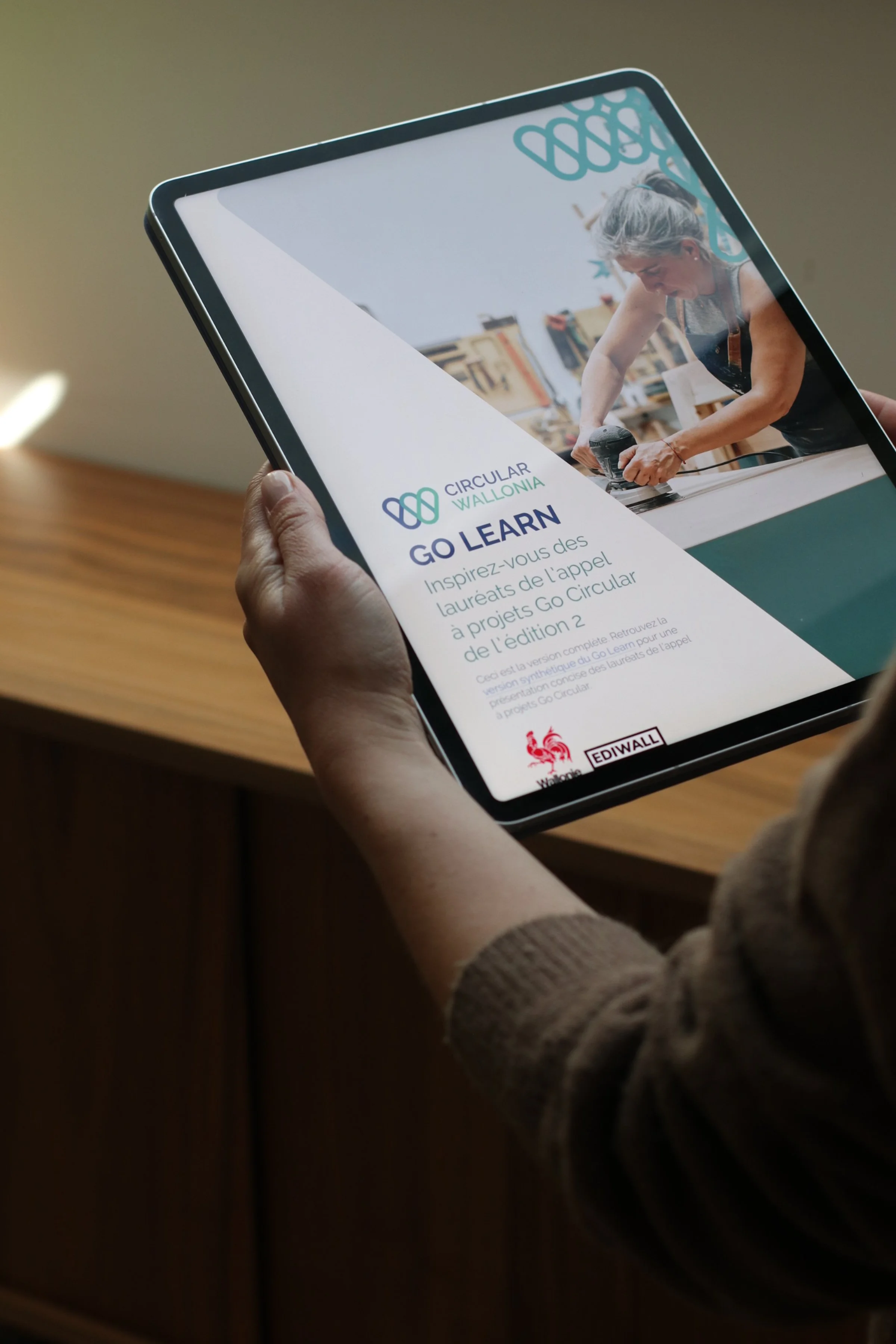 A person holding a tablet displaying a color guide with various color swatches and images of a brick building, over a white surface.