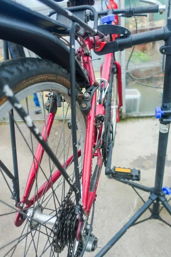 A red bicycle mounted on a repair stand with a blue cap water bottle attached to the frame, in a workshop or garage setting.
