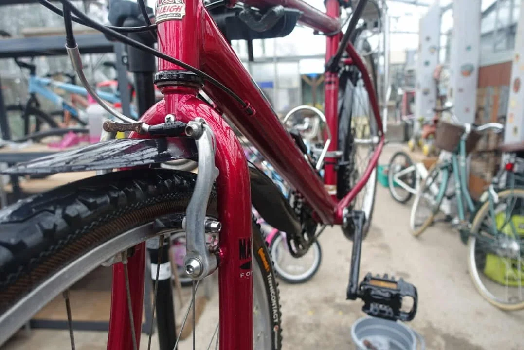 Close-up of a red bicycle with a focus on the front fork and tire, with other bicycles visible in the background.