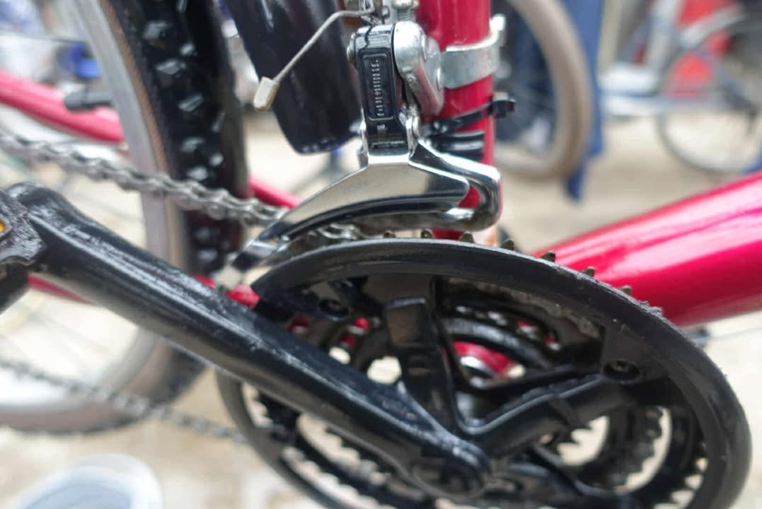 Close-up of a bicycle's drivetrain showing the chain, front derailleur, and chainring on a red bike frame.