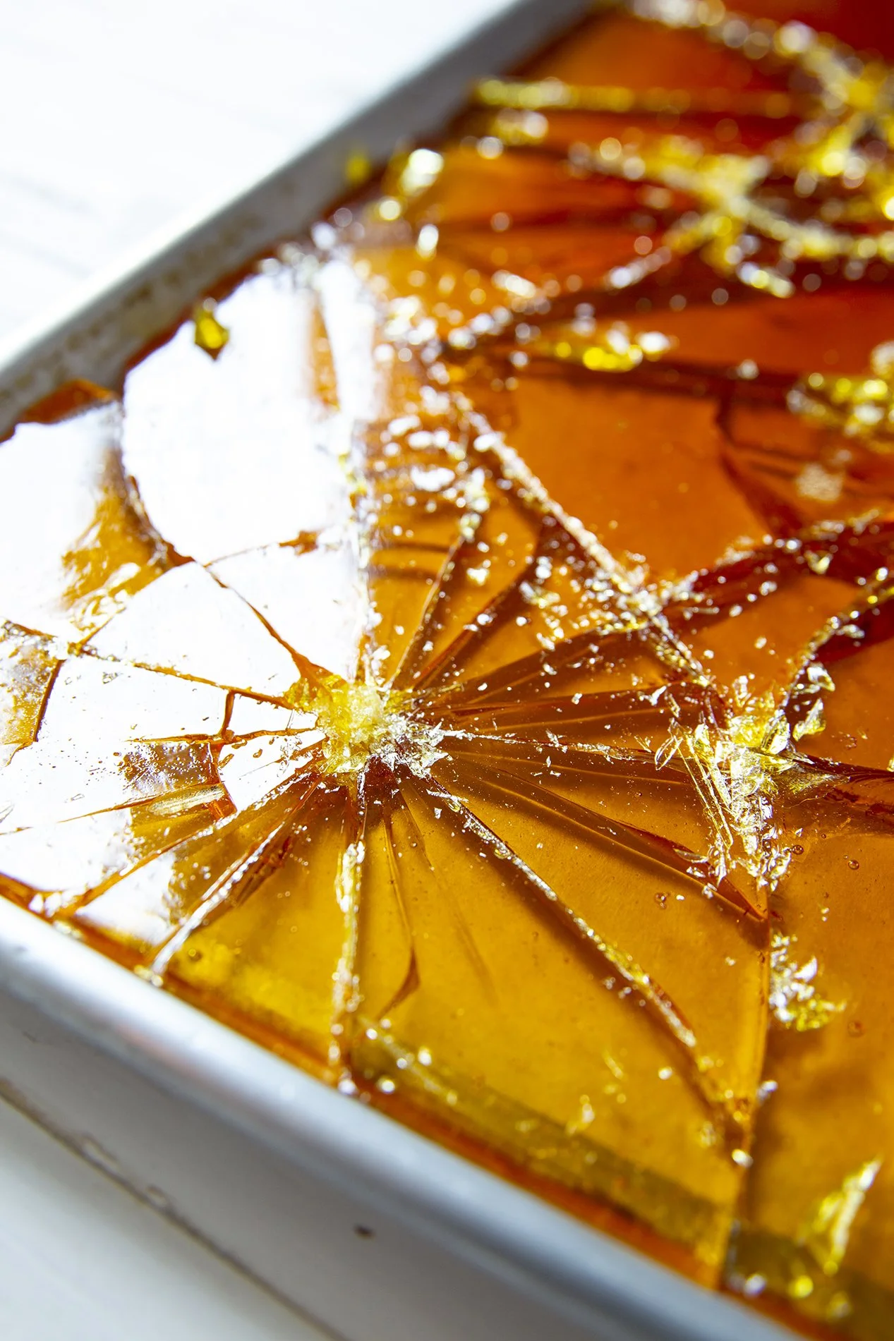 Close-up of shattered Breton caramel on baking tray, cracks catching the golden light 
