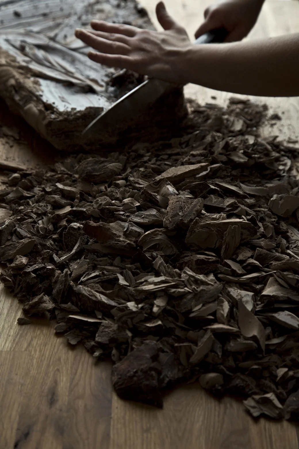 Hands holding a large chef's knife chopping a slab of dark chocolate on wooden butcher block