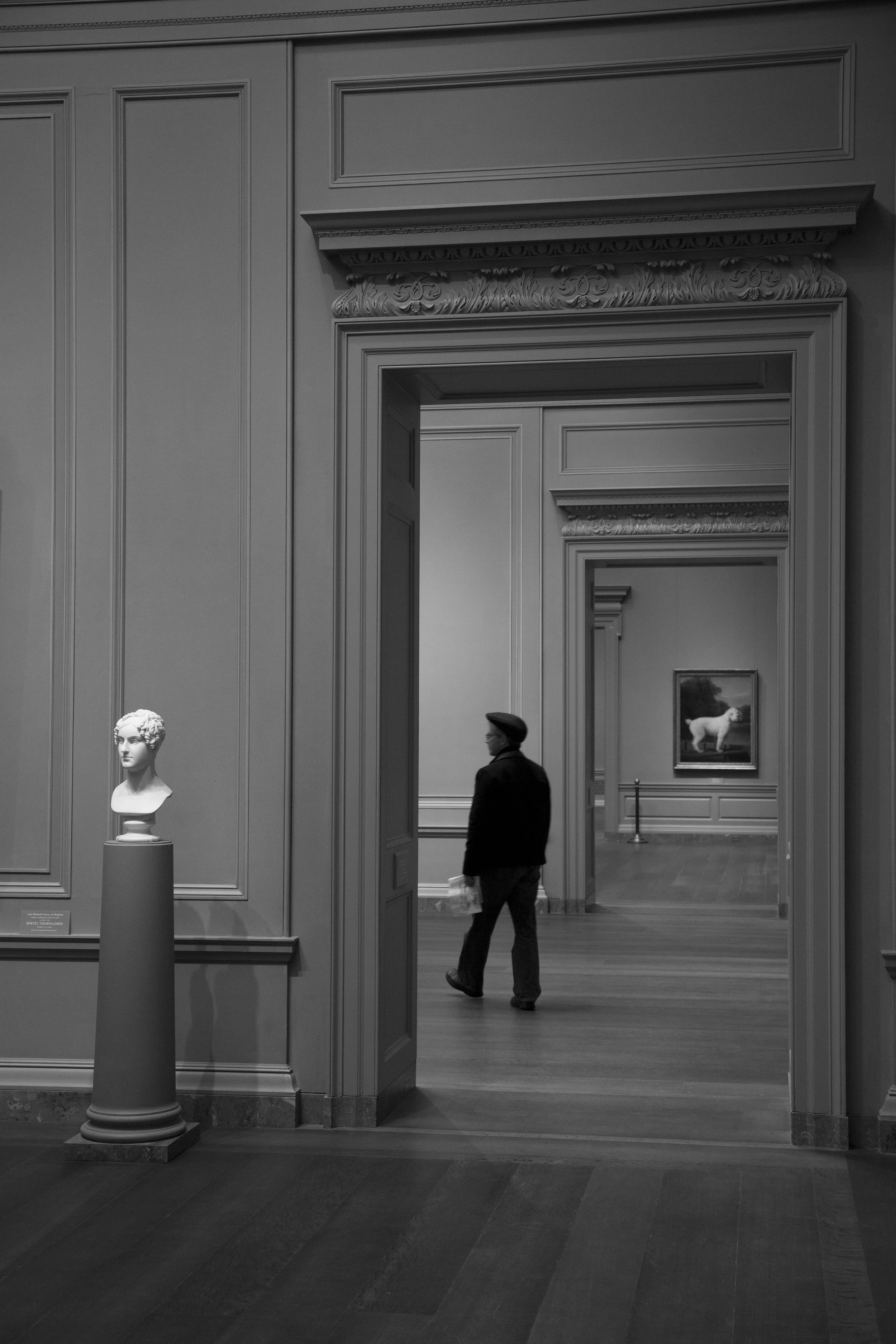 Art museum with guard walking by and statues, architectural perspective with doors within doors, moody lighting