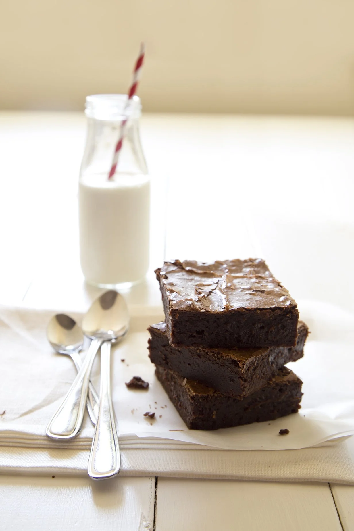 Triple chocolate brownie, piled on a wooden table, with a white bottle of milk and red straw in the background