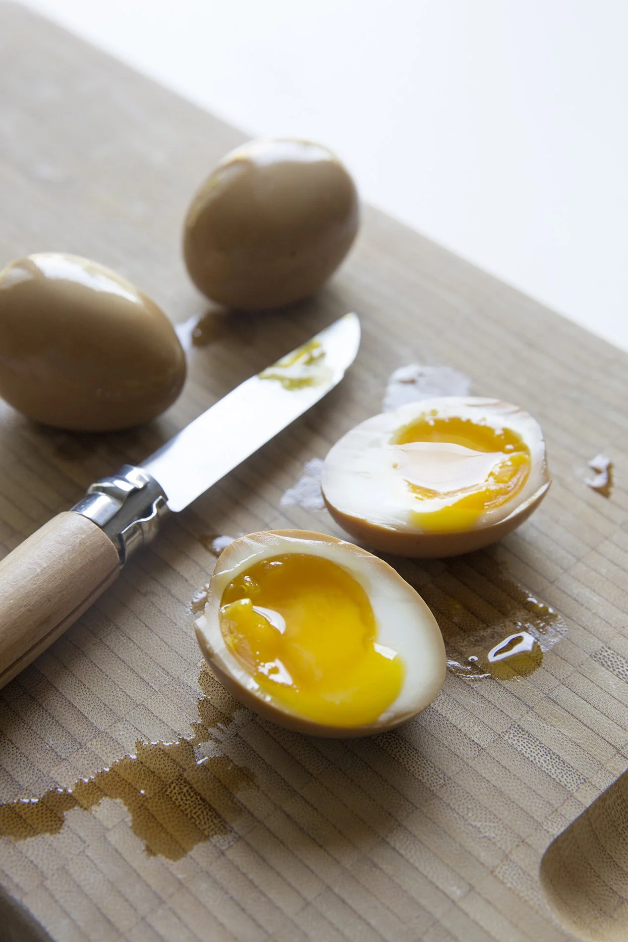 Soft-boiled ramen eggs colored by soy sauce, one egg cut open to show the liquid yellow yolk