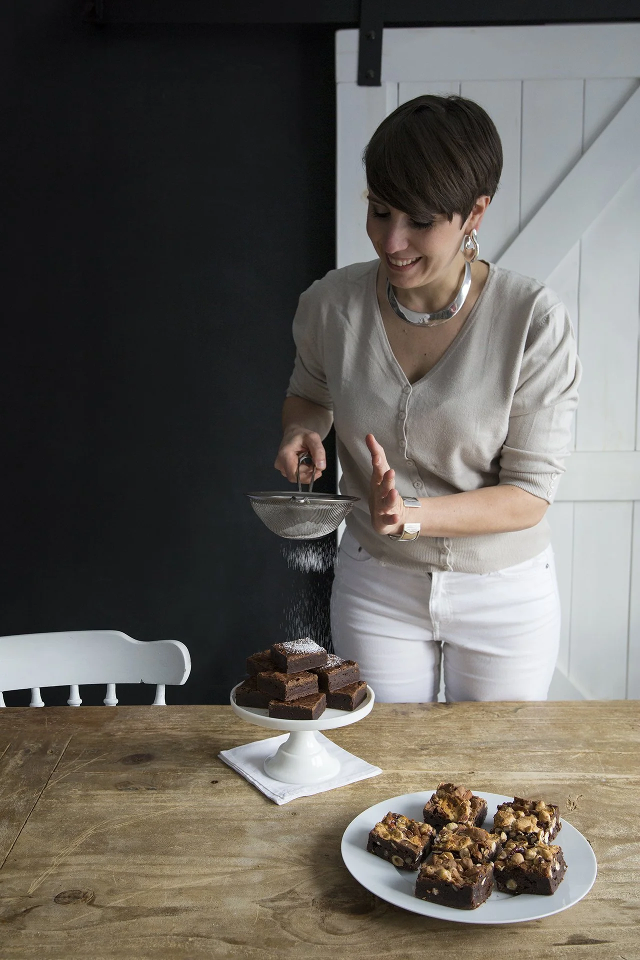 The chef Juliette Brun in her home kitchen smiling and dusting with sugar a plate of brownies