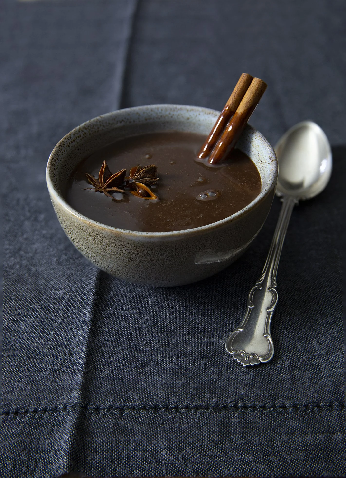 A bowl of spiced drinking chocolate with cinnamon and anis seeds, with beautiful silver spoon on blue background