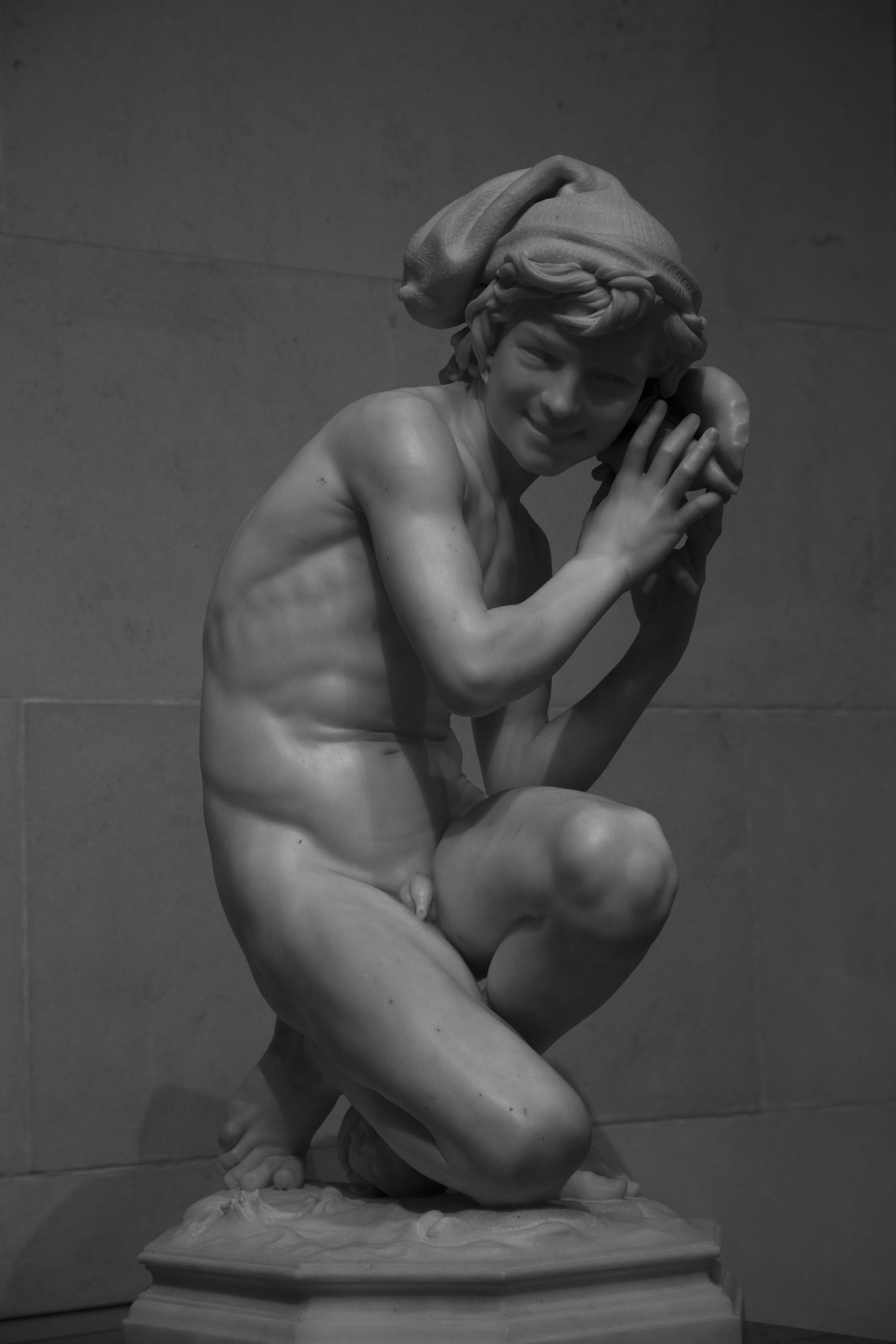 Stone statue of impish boy smiling, art museum scene captured in black and white photo. 