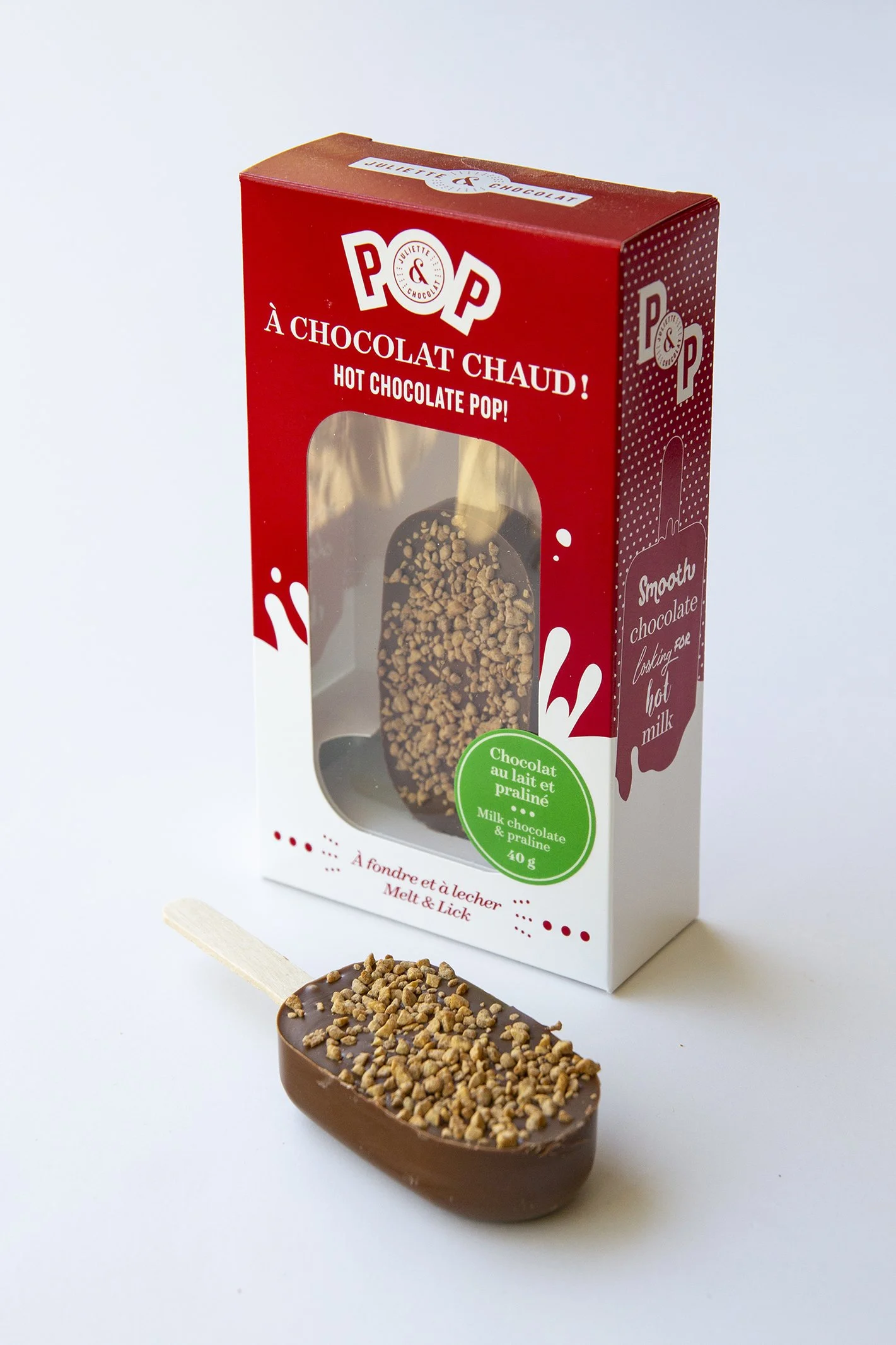 Lollipop made of milk chocolate with crunchy roasted hazelnut bits and its red retail box. 