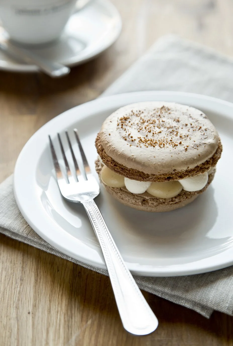 Large french macaron filled with maple and vanilla creams, on beautiful serving plate with fork, dusted with cocoa