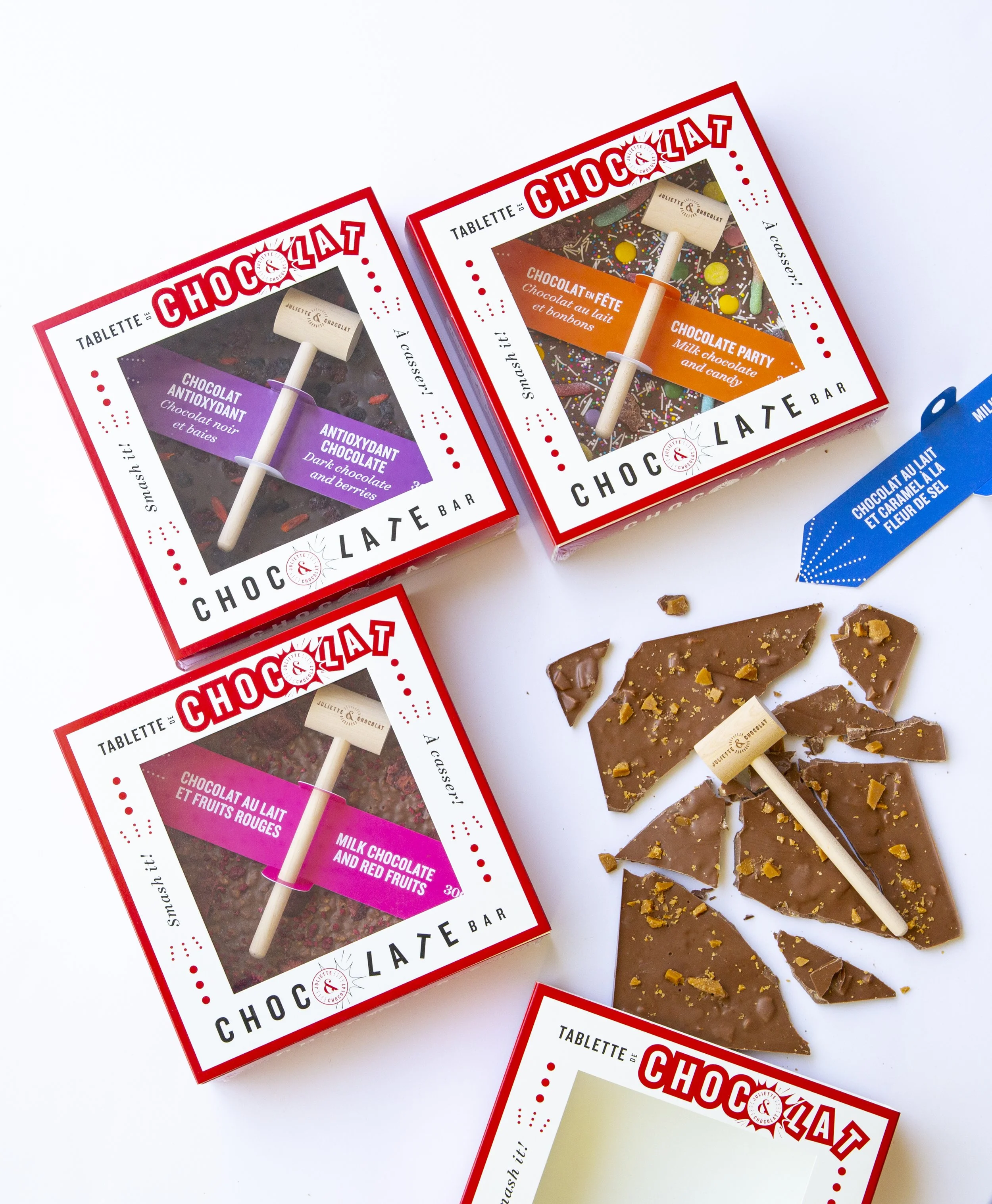 Four large chocolate bars in different flavors and colorful packaging with small wooden hammers to break the chocolate.
