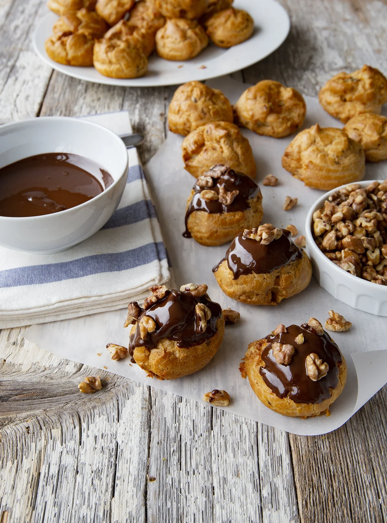Profiteroles dipped in shiny dark chocolate and with chopped hazelnuts, on rustic wooden background.
