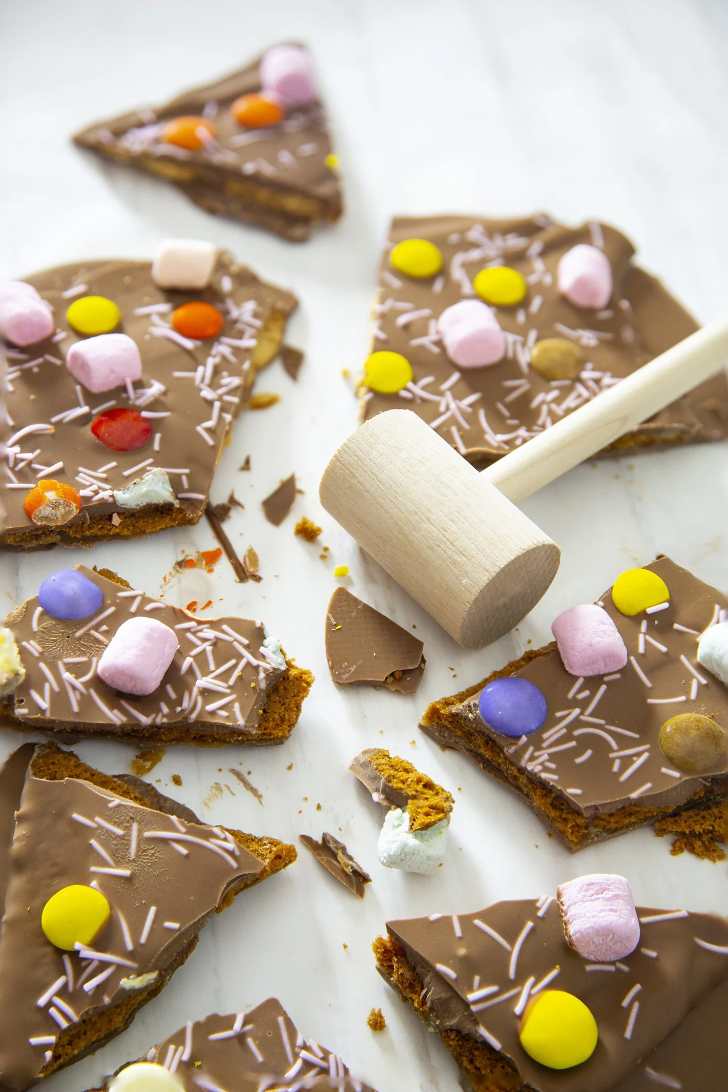 Easter milk chocolate bark with candies and marshmallows, broken in wooden table with small wooden mallet. 