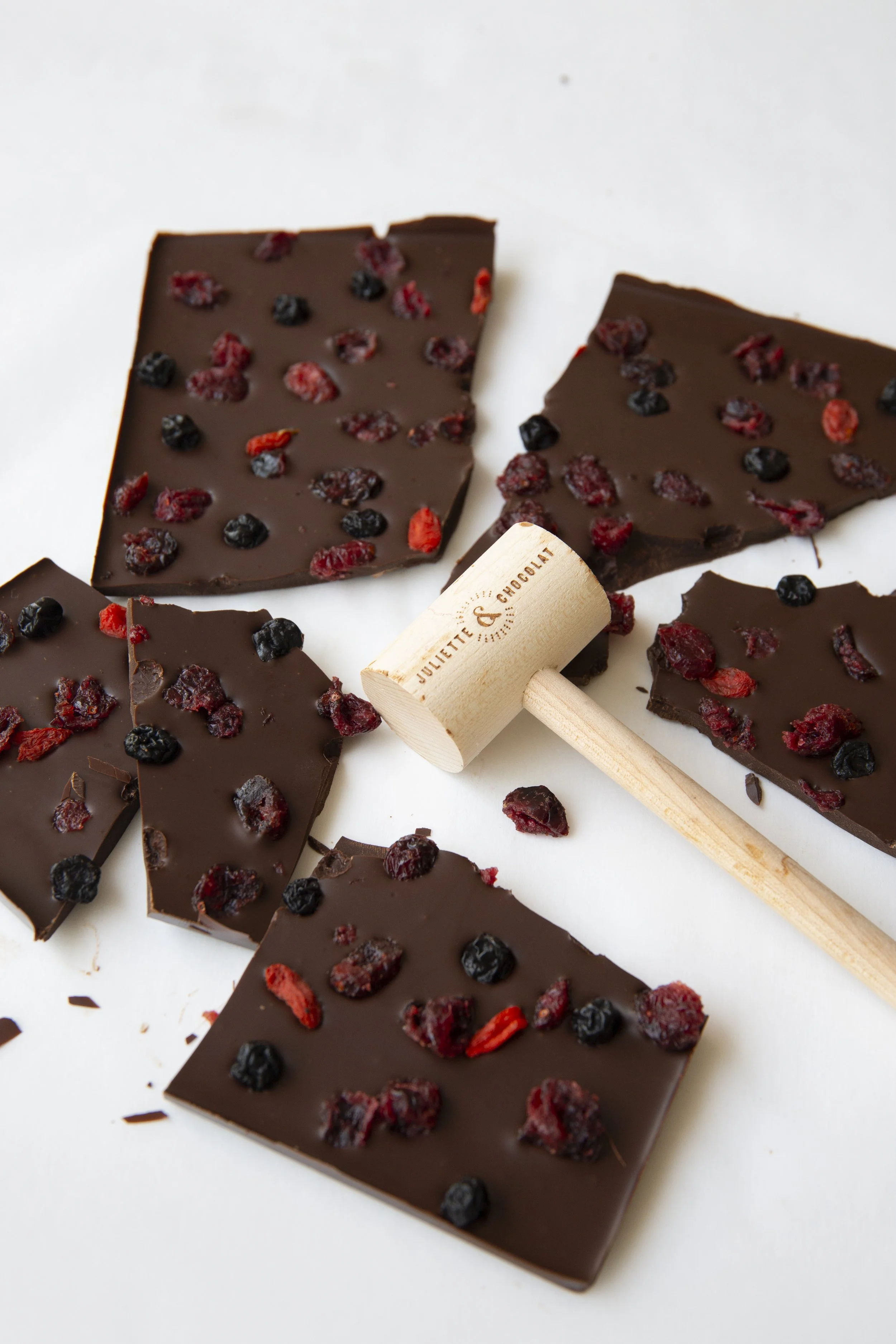 Dark chocolate bar with red berry inclusions, and small wooden mallet with the inscription Juliette & Chocolat. 
